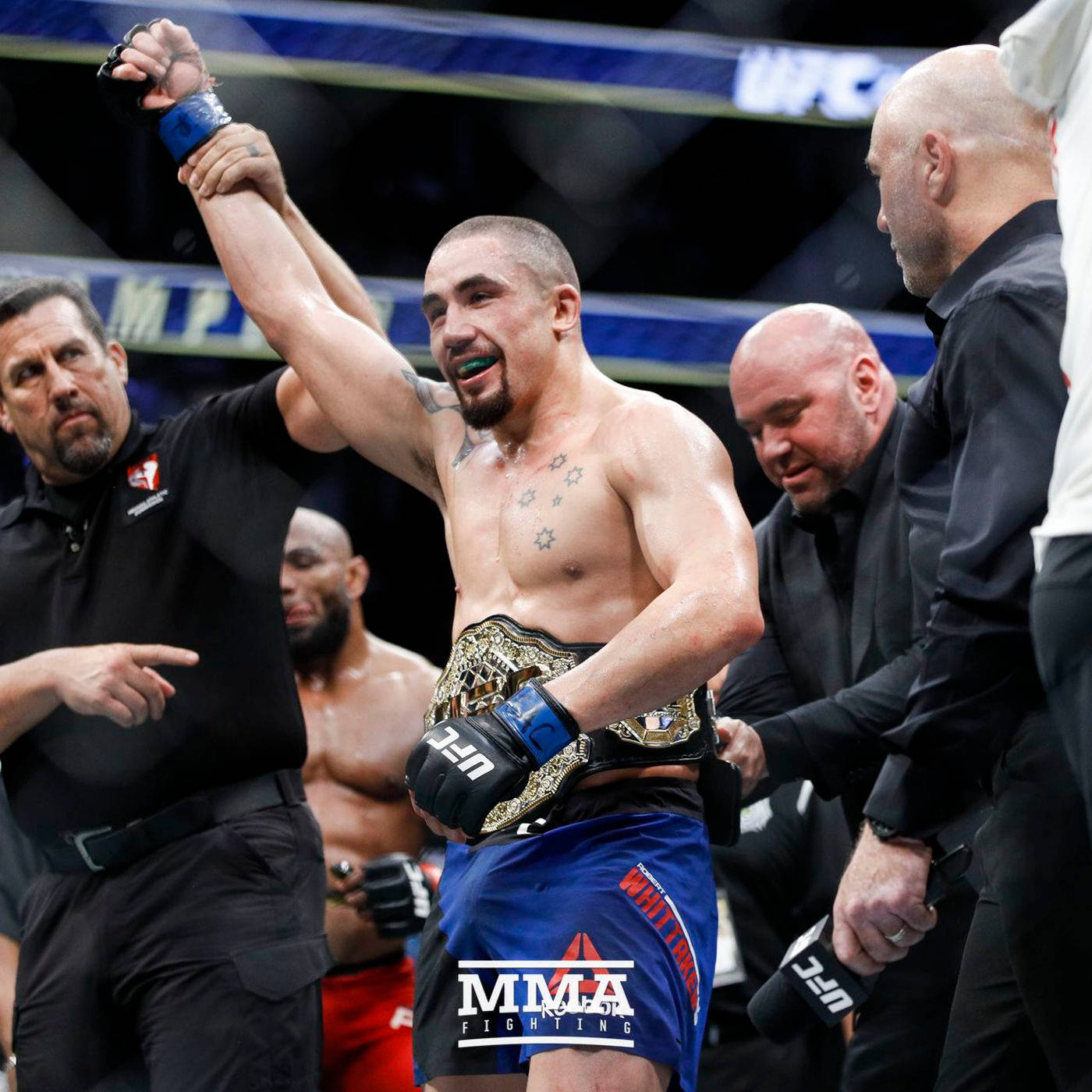 Victory 桌布 壁紙 — 一位勝利的MMA拳手在八角籠中由官員舉起手臂慶祝，同時佩戴冠軍腰帶。