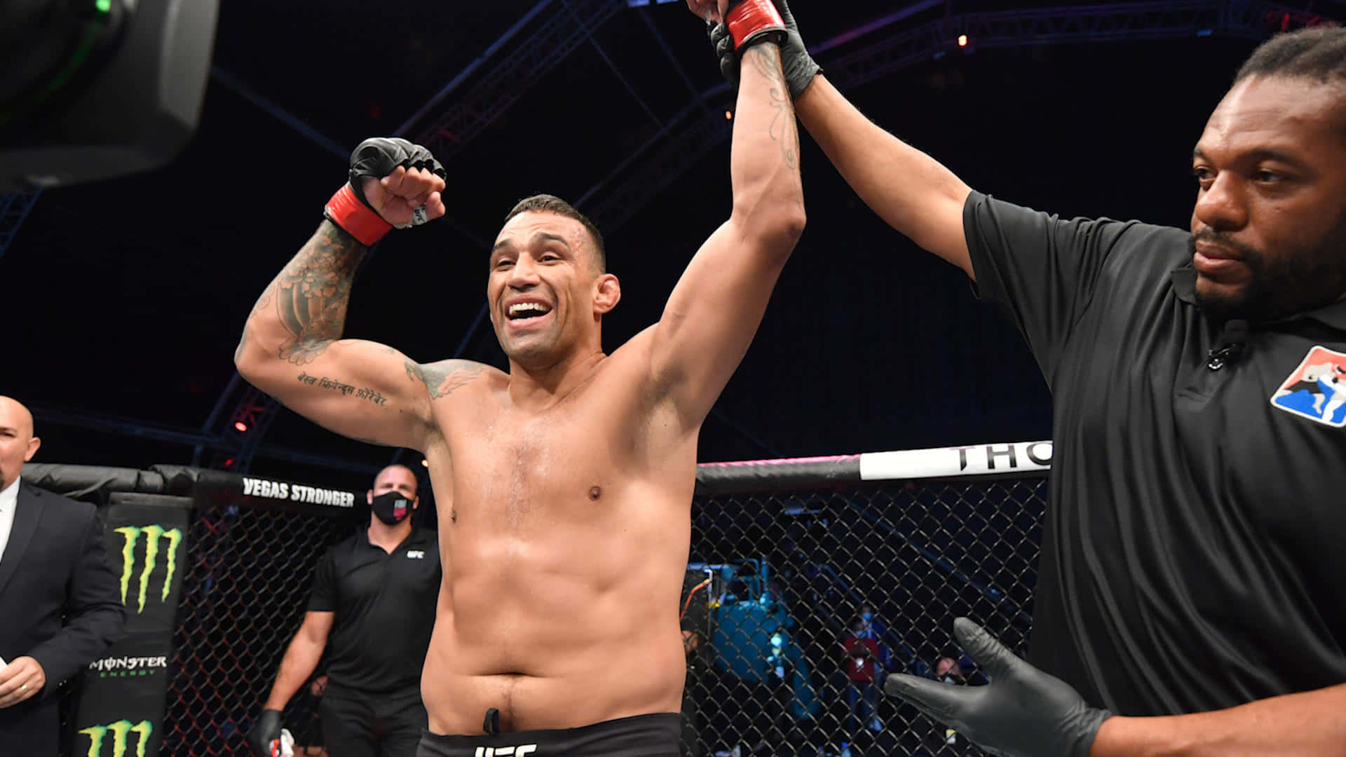 UFC 桌布 壁紙 — 一位勝利的MMA拳手在八角籠內慶祝，裁判在明亮的場館燈光下舉起他的手臂。