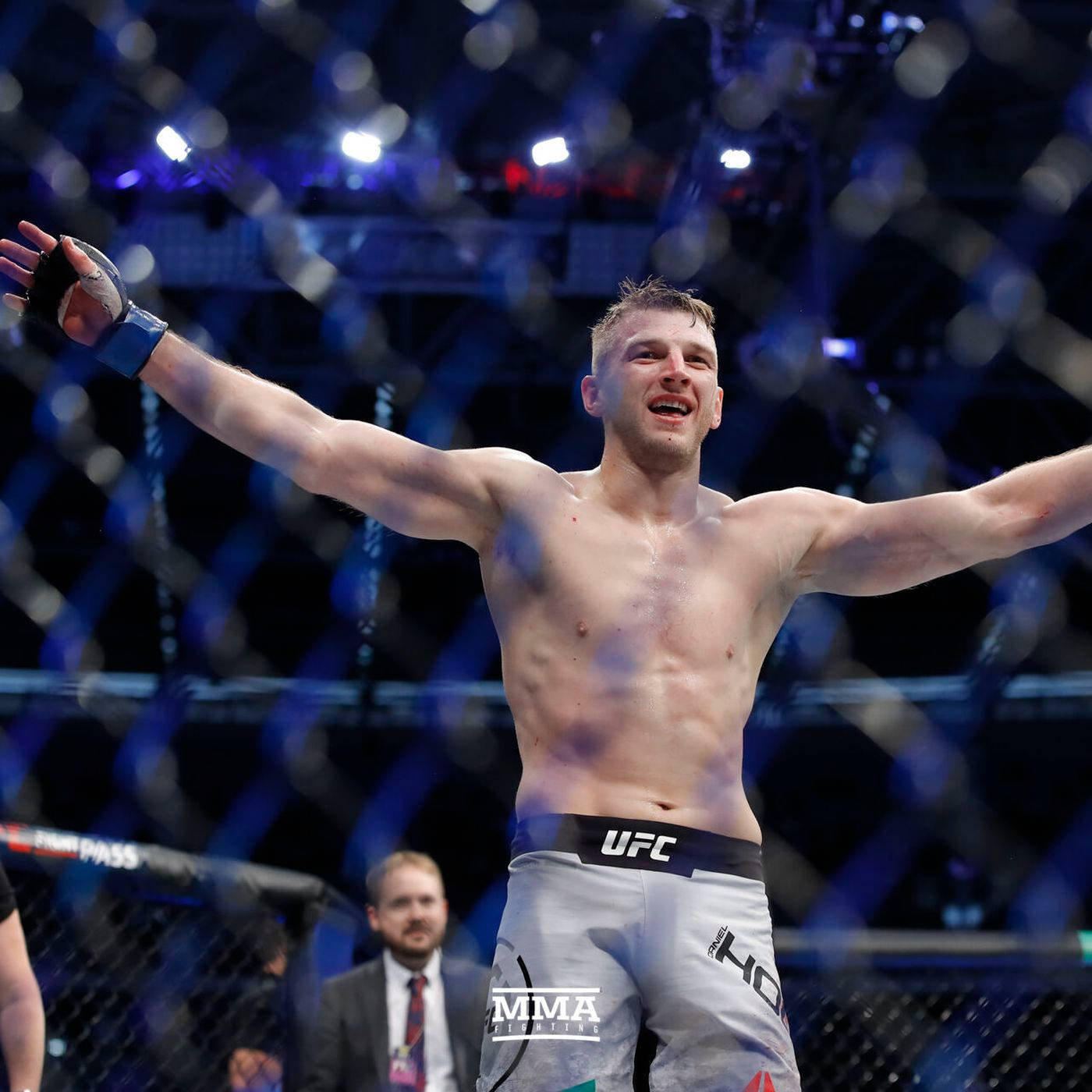 UFC 桌布 壁紙 — 一位勝利的MMA拳手在燈光明亮的八角籠內張開雙臂慶祝。