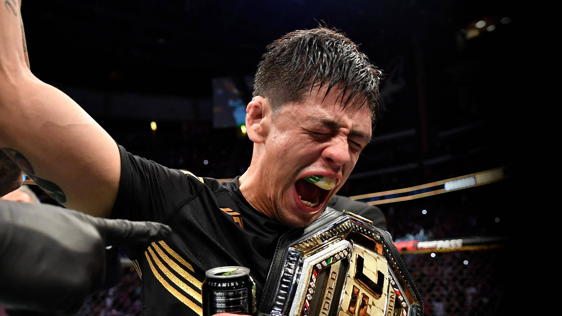 Brandon Moreno 桌布 壁紙 — 一位勝利的MMA拳手高聲歡呼，手持冠軍腰帶和一罐維他命水。