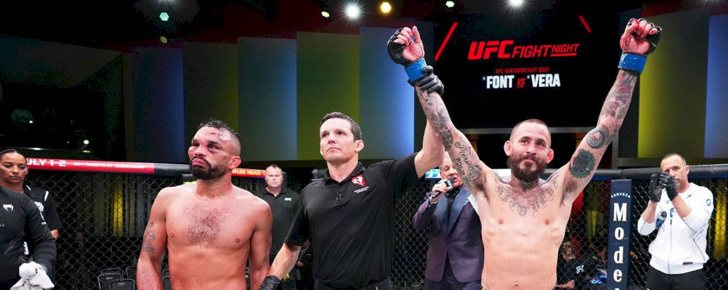 UFC 桌布 壁紙 — 一位勝利的UFC拳手，手臂上有刺青，在裁判宣布他在八角籠中獲勝時舉起拳頭。