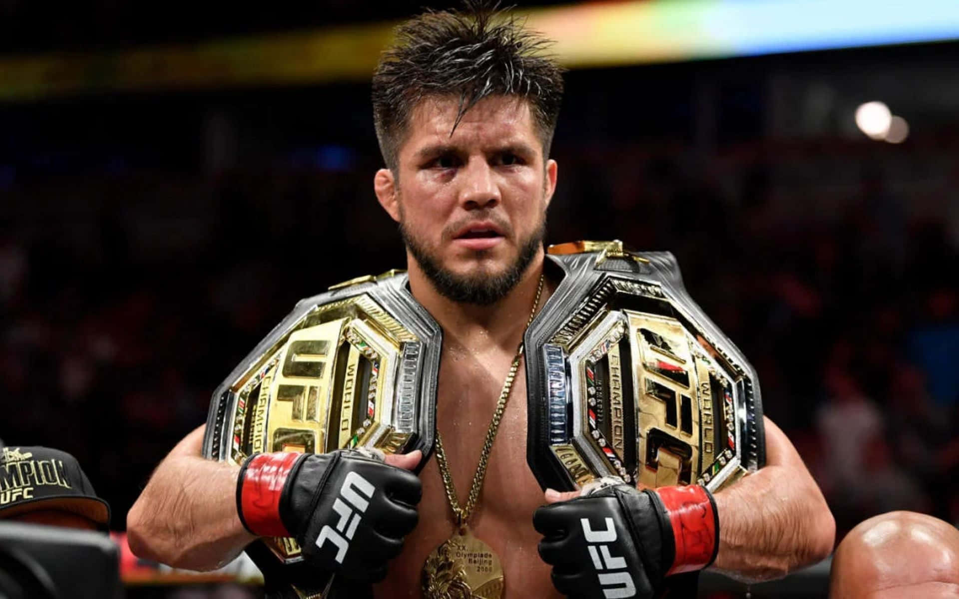 UFC 桌布 壁紙 — 一位勝利的UFC拳手，臉上閃爍著汗水，在明亮的競技場中將兩條冠軍腰帶扛在肩上。
