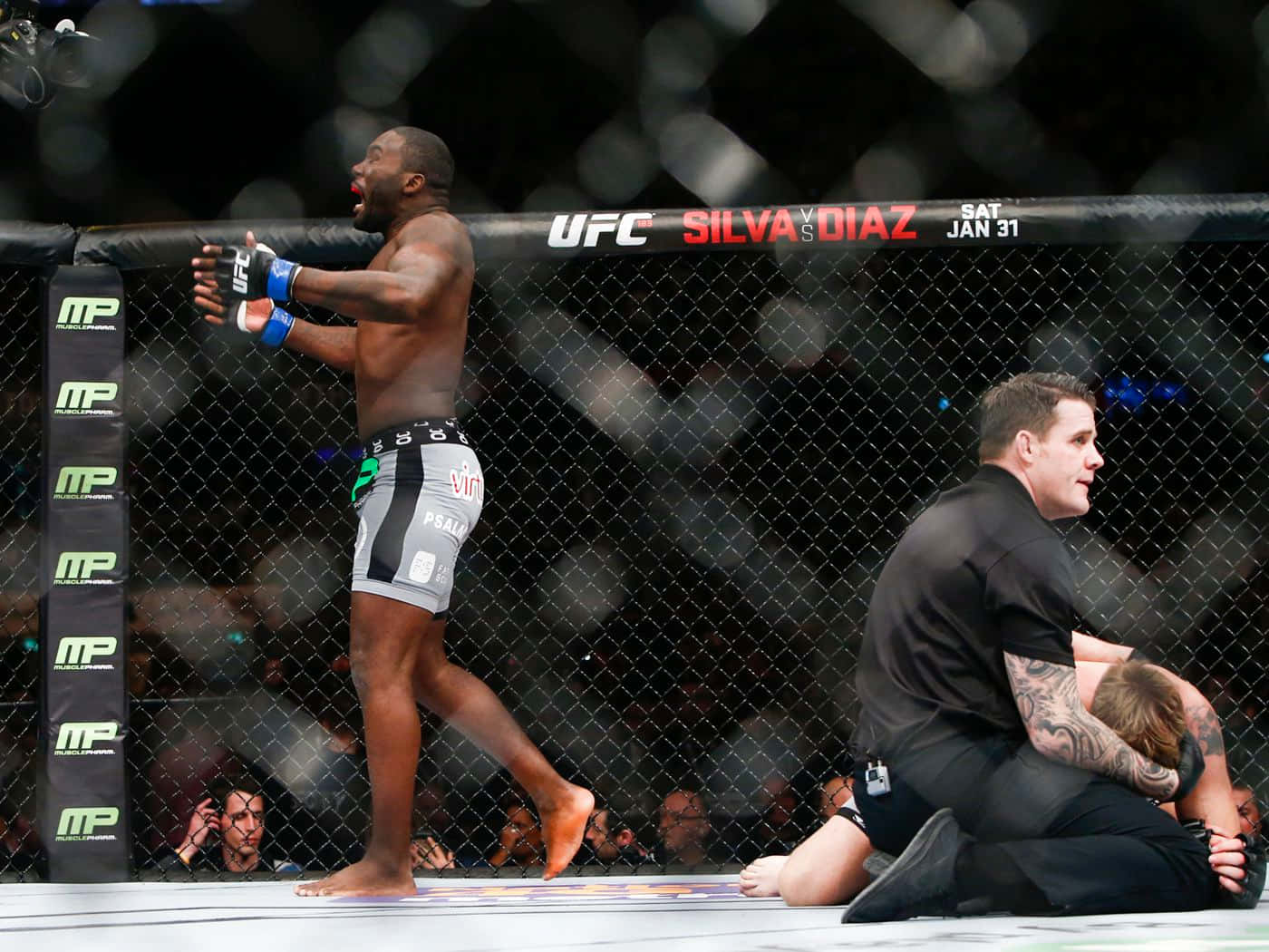 UFC 桌布 壁紙 — 一位勝利的UFC拳手在八角籠中慶祝，而裁判正在照顧他的對手。