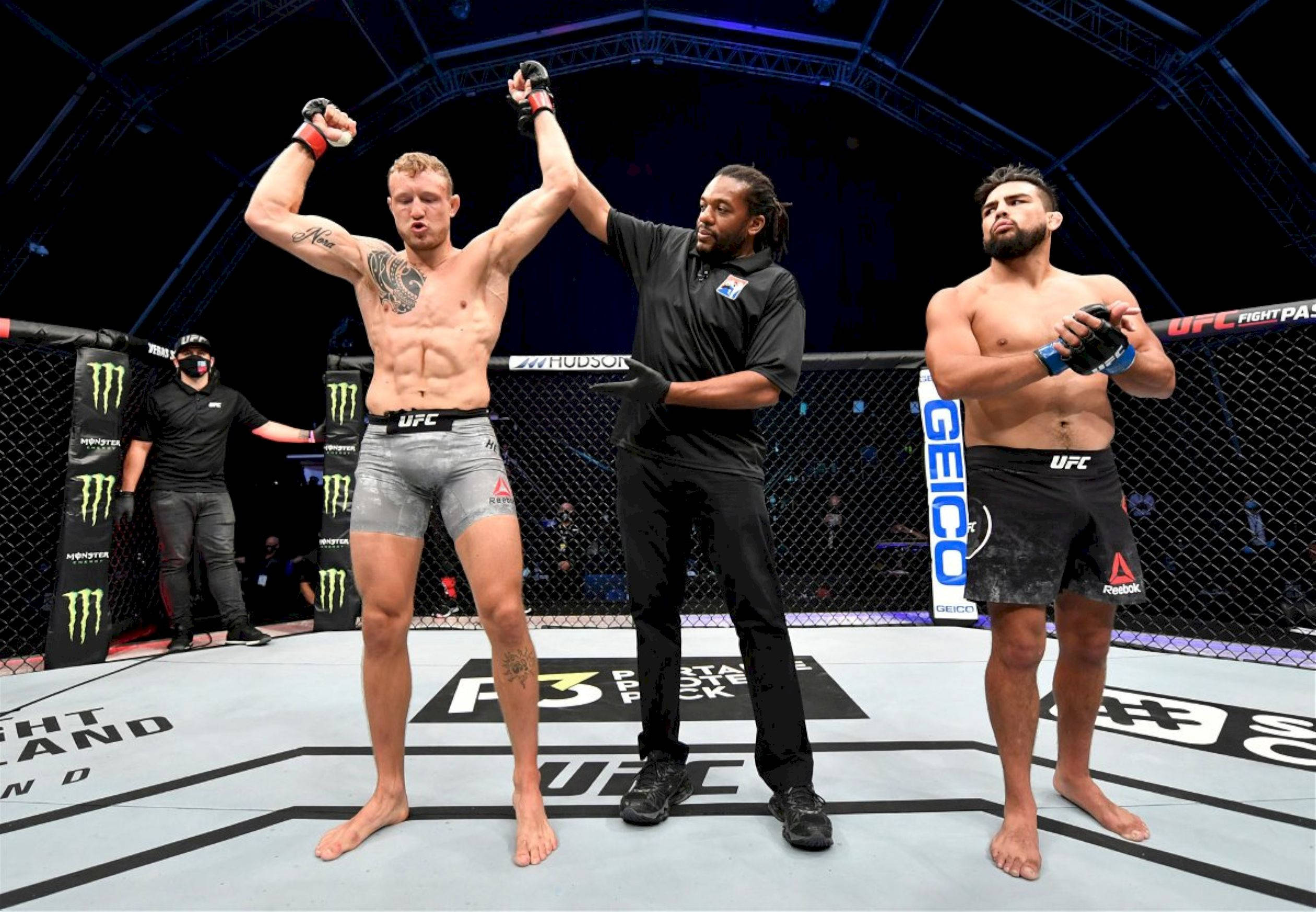 桌布 壁紙 — 一位勝利的UFC拳手在八角籠中高舉雙臂，裁判宣佈他為勝者，對手站在一旁。