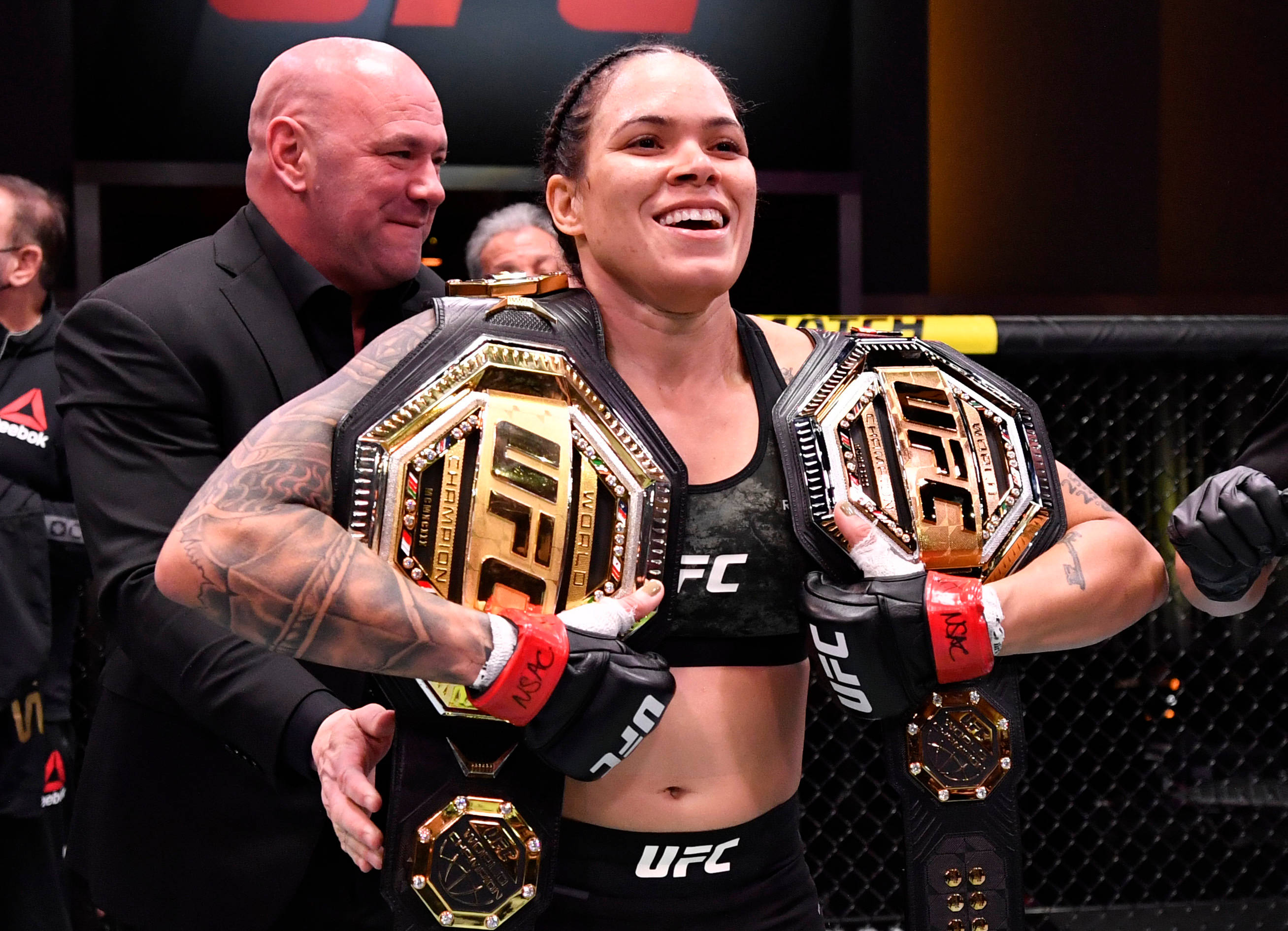 Victory 桌布 壁紙 — 一位勝利的UFC拳手在八角籠內自豪地展示兩條冠軍腰帶，滿臉喜悅。