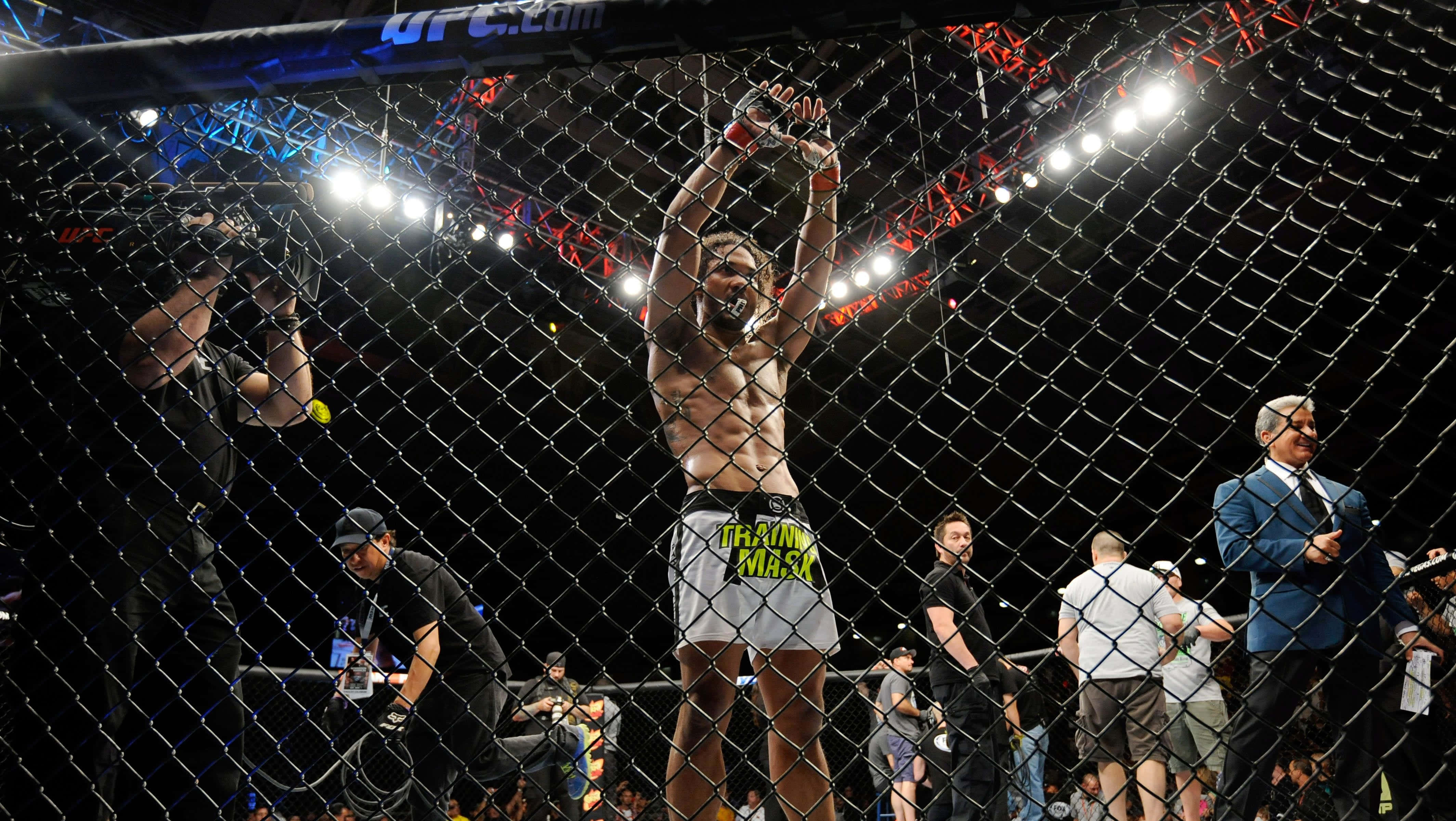 Fight 桌布 壁紙 — 一位勝利的UFC拳手在八角籠內舉起雙臂慶祝，攝影師捕捉了這一刻。