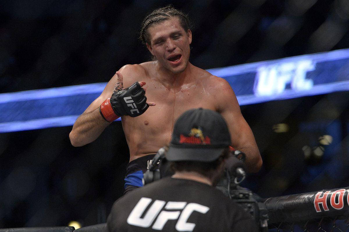 Brian Ortega 桌布 壁紙 — 一位勝利的UFC拳手在八角籠內豎起大拇指慶祝，同時攝影團隊正在拍攝他。