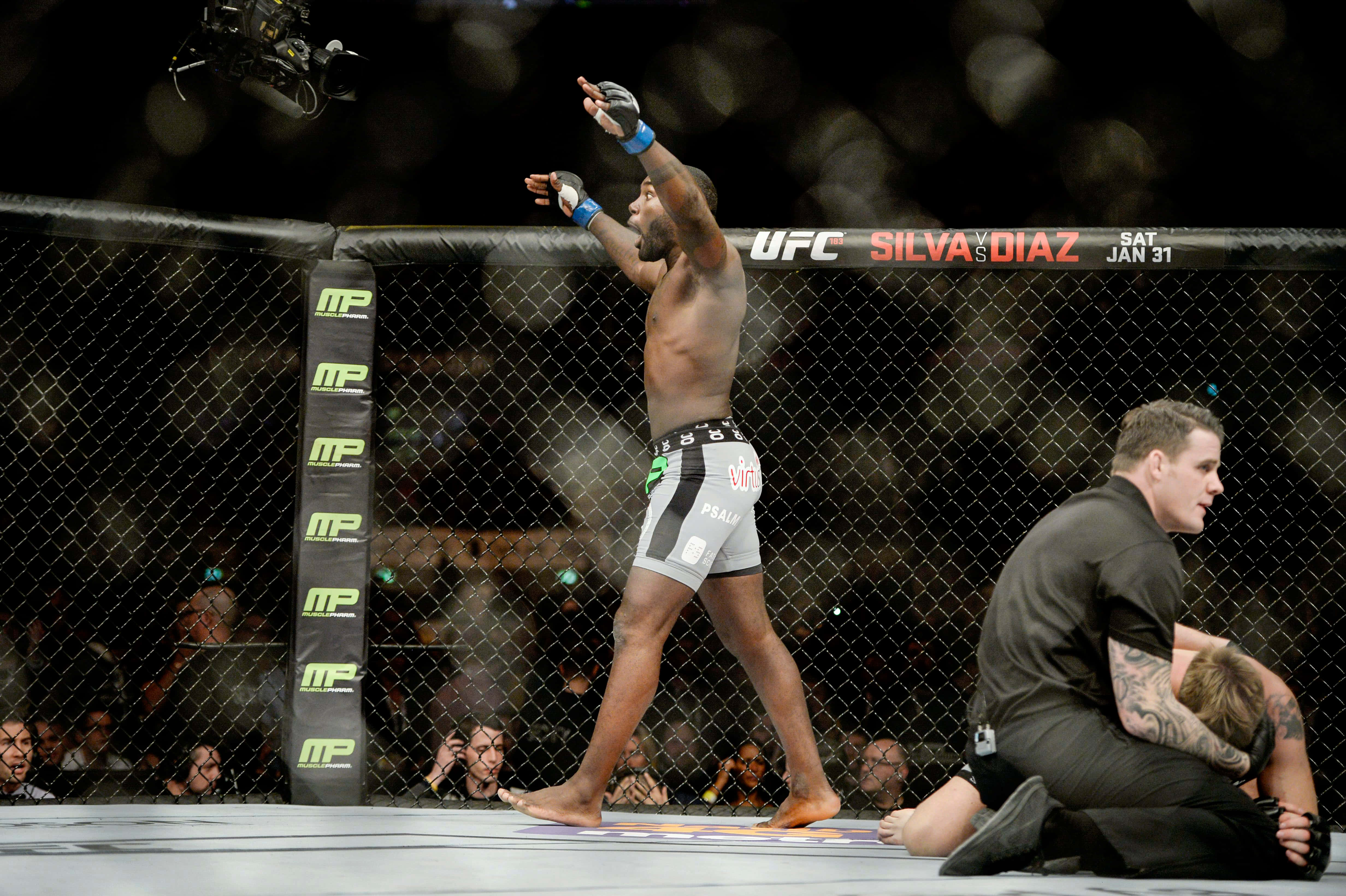 MMA 桌布 壁紙 — 一位勝利的UFC拳手在八角籠內高舉雙臂慶祝勝利，而他的對手正由裁判協助。