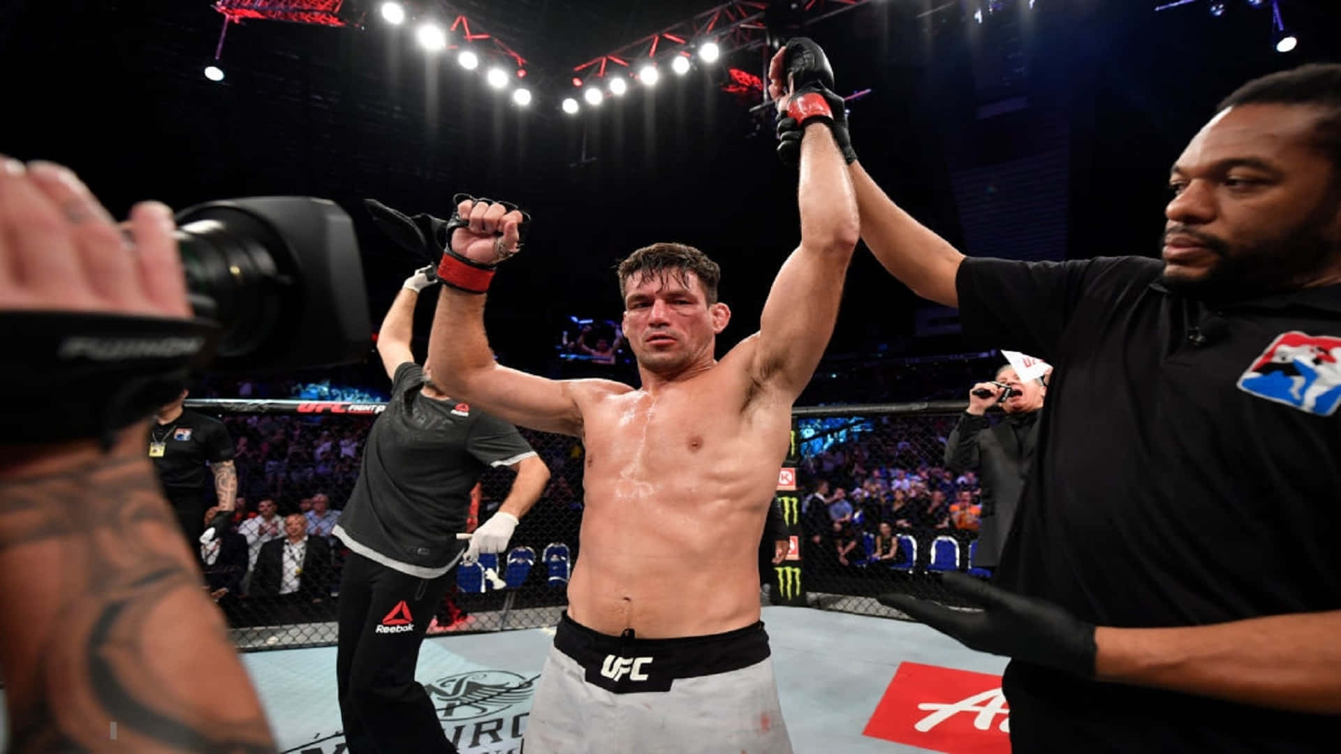 Champion 桌布 壁紙 — 一位勝利的UFC拳手在八角籠內高舉雙臂慶祝勝利，裁判也舉起他的手，場館燈光璀璨。
