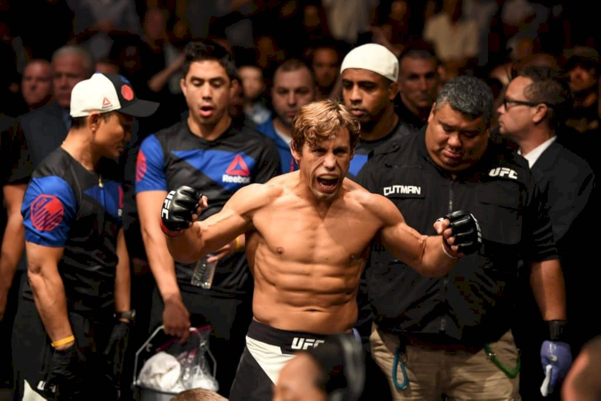 UFC 桌布 壁紙 — 一位勝利的UFC拳手在八角籠內高舉雙臂，發出勝利的吶喊，他的團隊和官員圍繞著他。