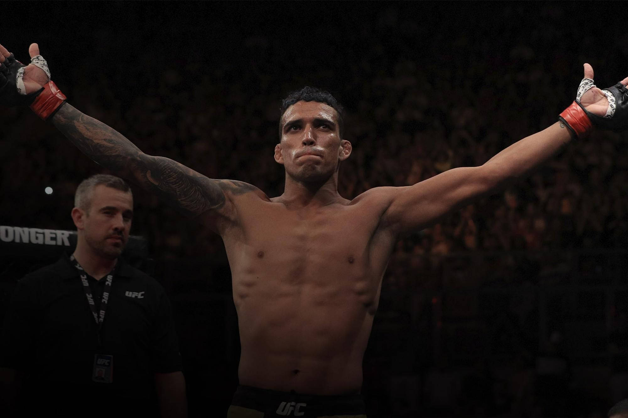 MMA 桌布 壁紙 — 一位勝利的UFC拳手在場館燈光下高舉雙臂慶祝勝利，裁判在他身旁。