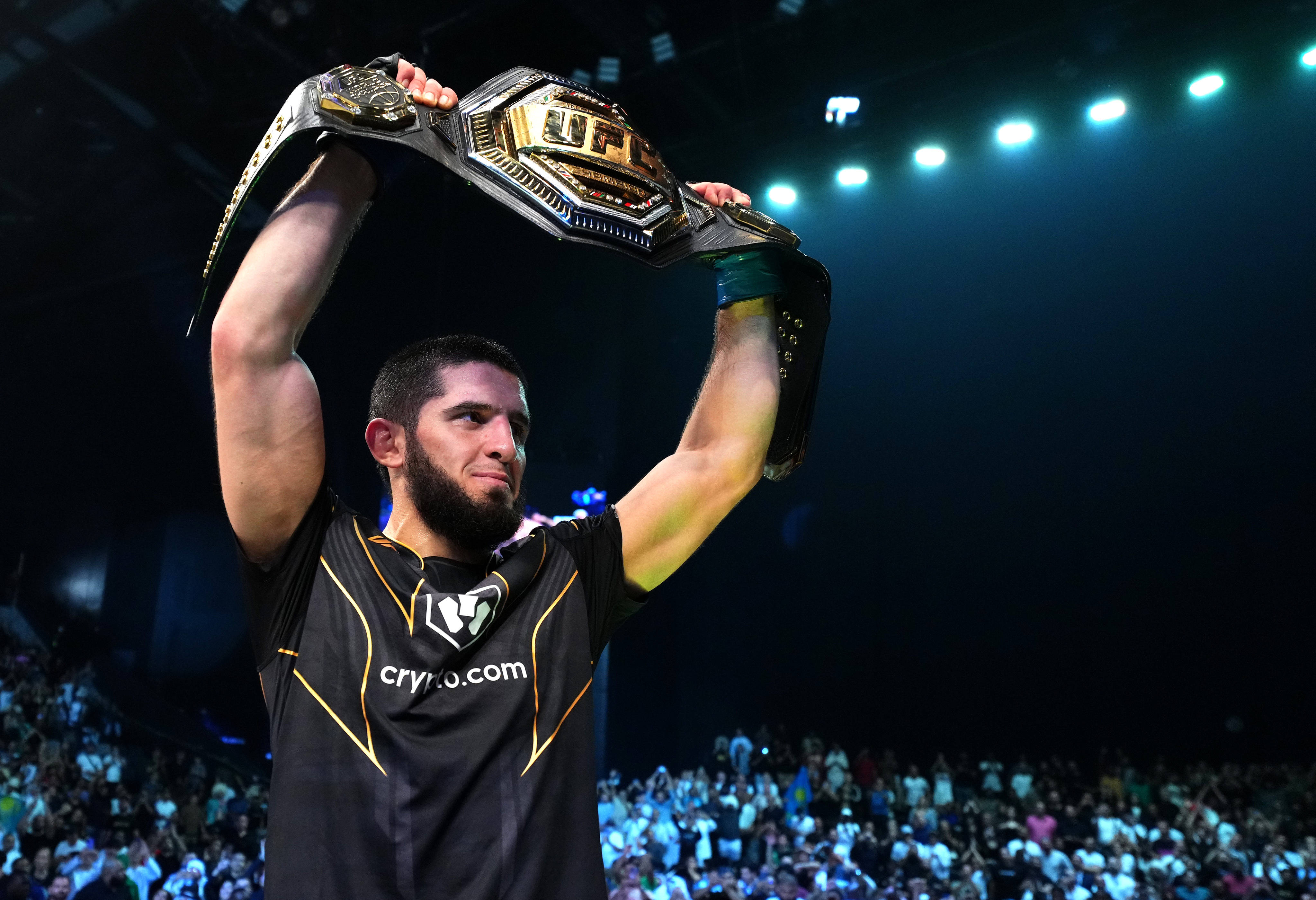 Champion 桌布 壁紙 — 一位勝利的UFC拳手在場館燈光下將冠軍腰帶高舉過頭，下方是歡呼的人群。