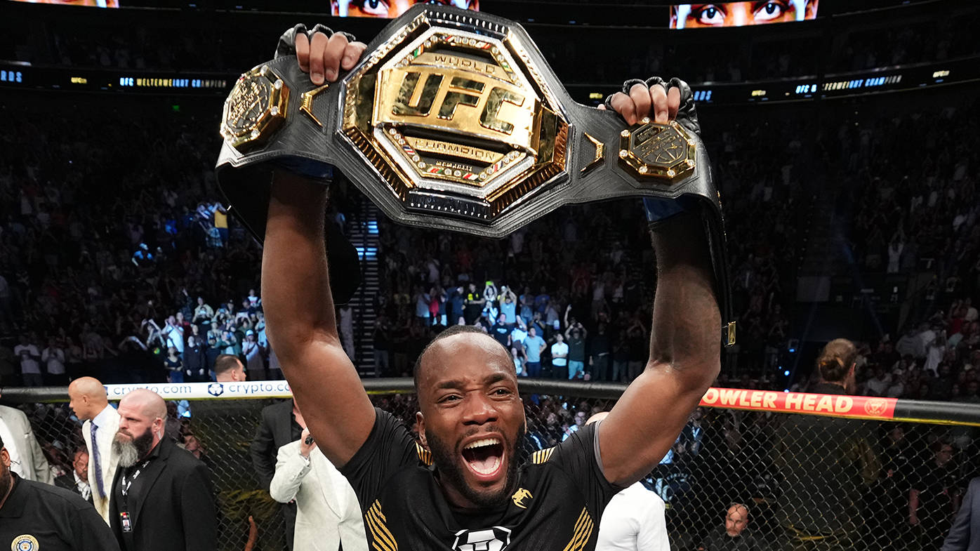 Champion 桌布 壁紙 — 一位勝利的UFC拳手在擠滿人的八角籠內高舉冠軍腰帶慶祝勝利。