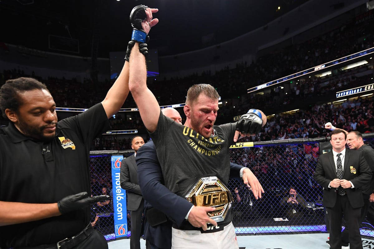 UFC 桌布 壁紙 — 一位勝利的UFC拳手在擠滿觀眾的八角籠內，由裁判舉起手臂慶祝。