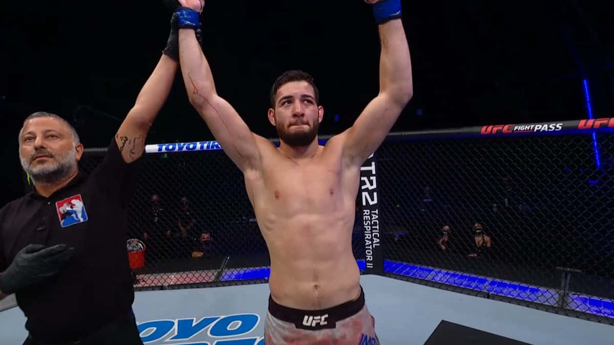 UFC 桌布 壁紙 — 一位勝利的UFC拳手在明亮的場館燈光下，在八角籠中高舉雙臂慶祝勝利，裁判舉起他的手。
