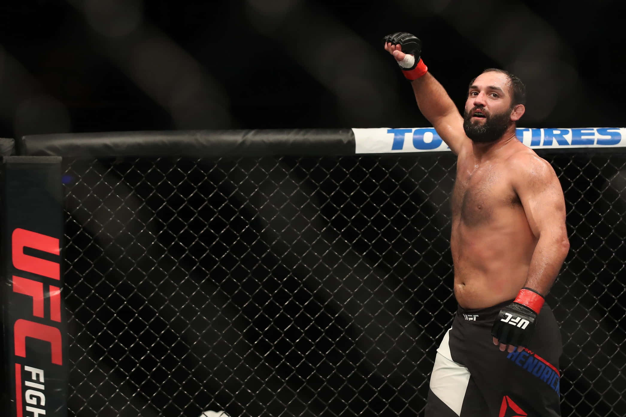 UFC 桌布 壁紙 — 一位勝利的UFC拳手在明亮的場館燈光下，於八角籠內高舉戴著手套的拳頭慶祝勝利。