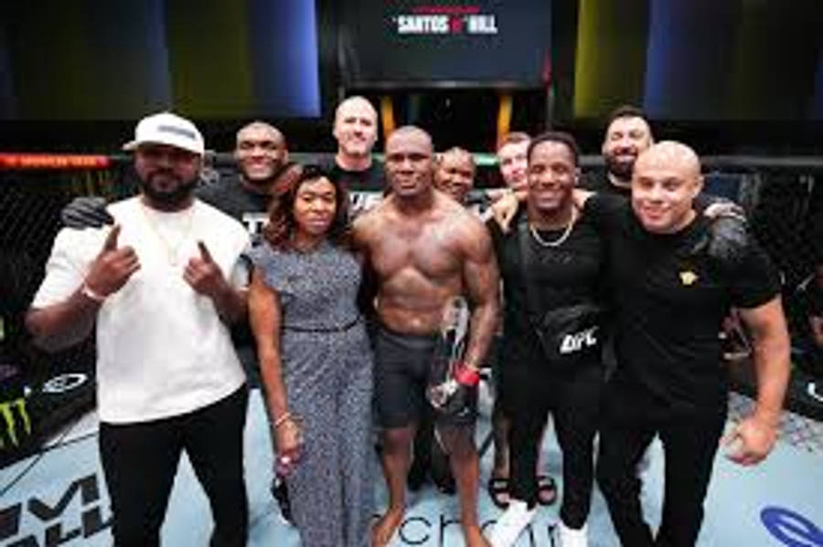 Kamaru Usman 桌布 壁紙 — 一位勝利的UFC拳手在明亮的場館燈光下，於八角籠內與團隊合影。