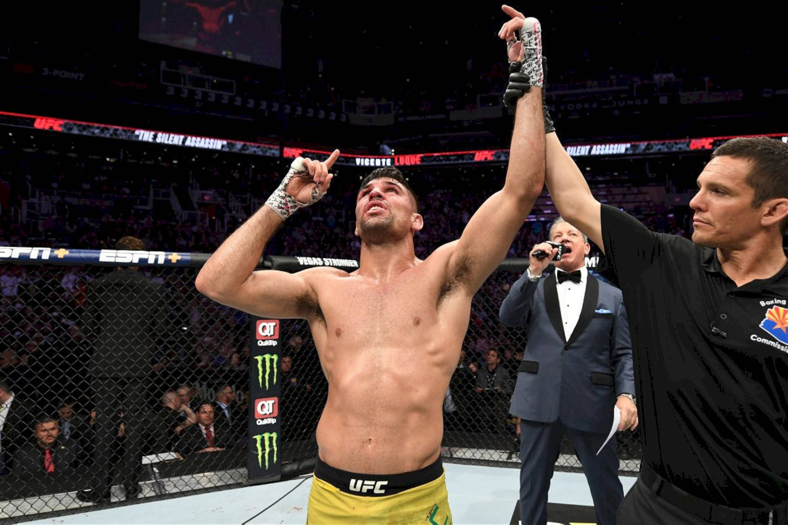 MMA 桌布 壁紙 — 一位勝利的UFC拳手在明亮的場館燈光下，於八角籠內慶祝，裁判舉起他的手臂。