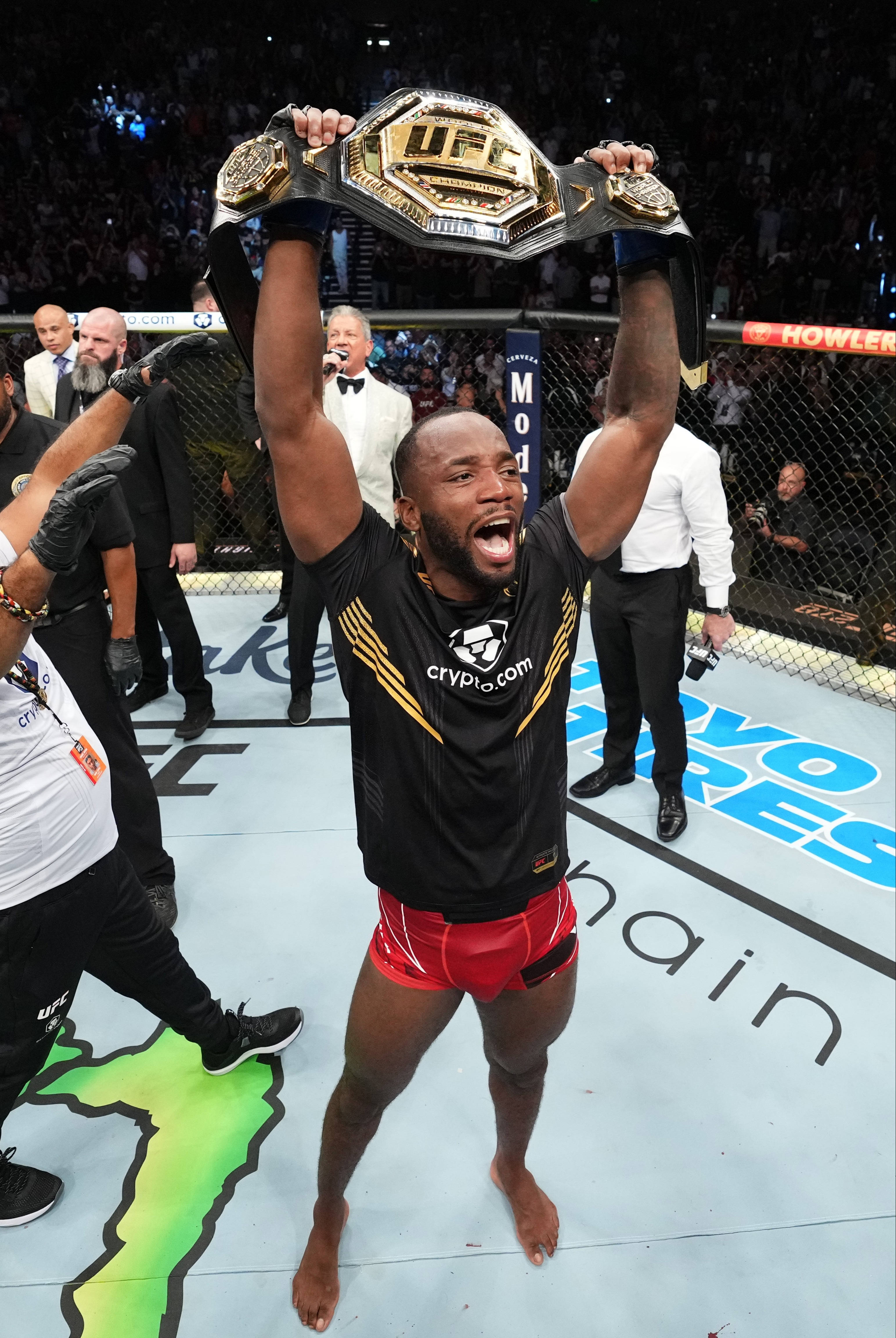 Champion 桌布 壁紙 — 一位勝利的UFC拳手在明亮的場館燈光下，在八角籠中勝利地將冠軍腰帶高舉過頭。