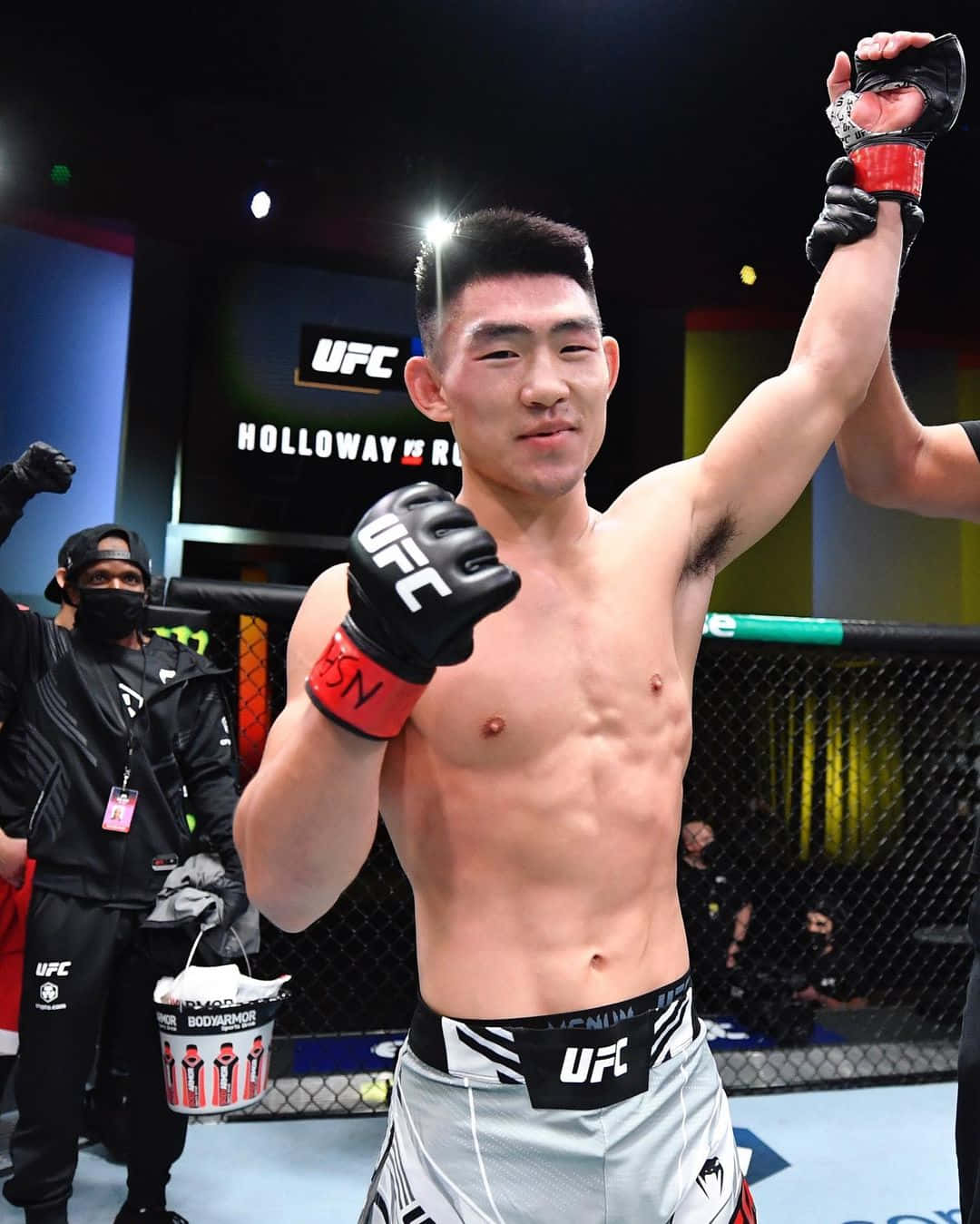 Athlete 桌布 壁紙 — 一位勝利的UFC拳手在明亮的場館燈光下，於八角籠內高舉手臂慶祝勝利。