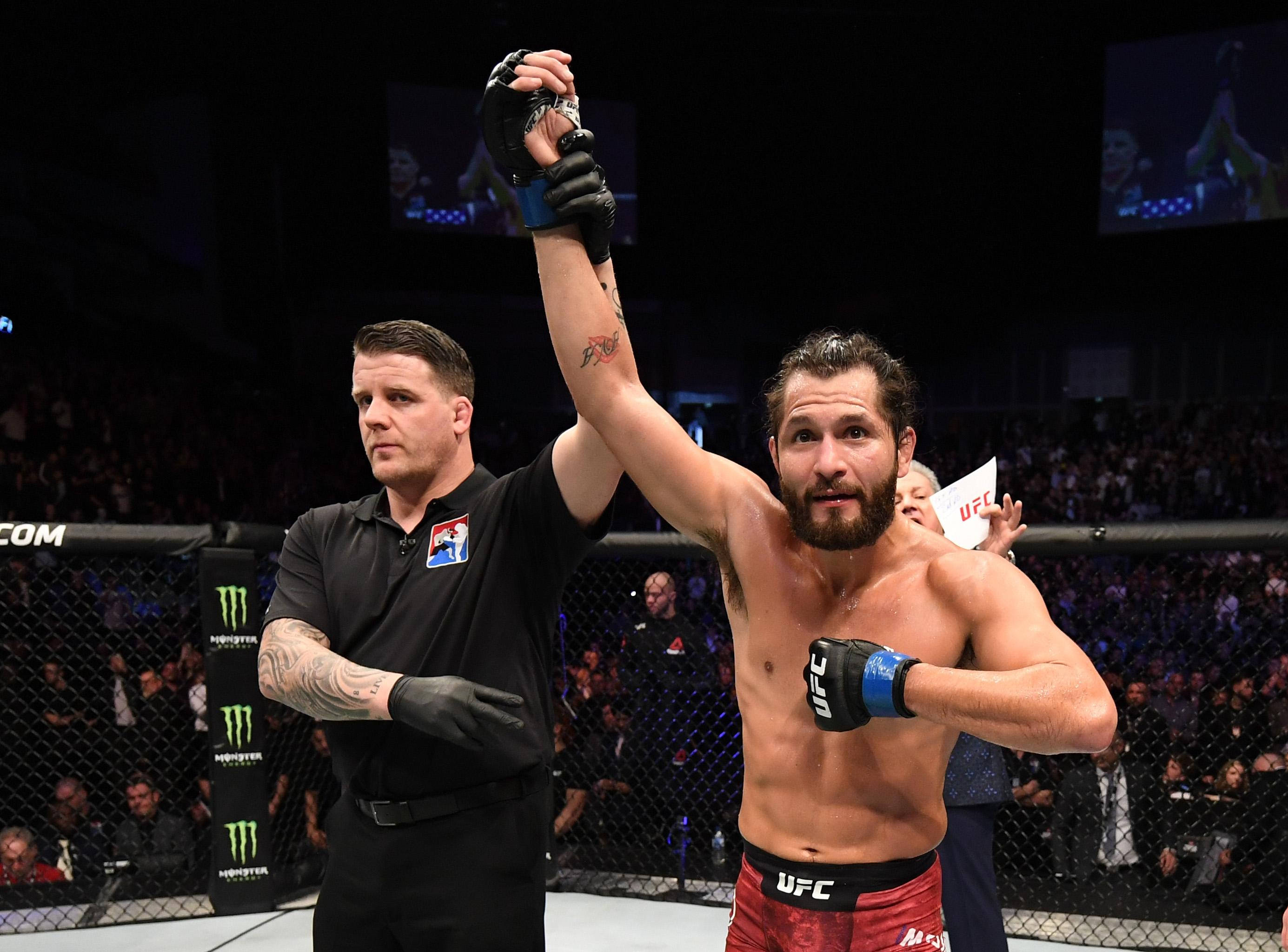 Victory 桌布 壁紙 — 一位勝利的UFC拳手在明亮的場館燈光下，於八角籠內被裁判宣佈為勝者時舉起手臂。