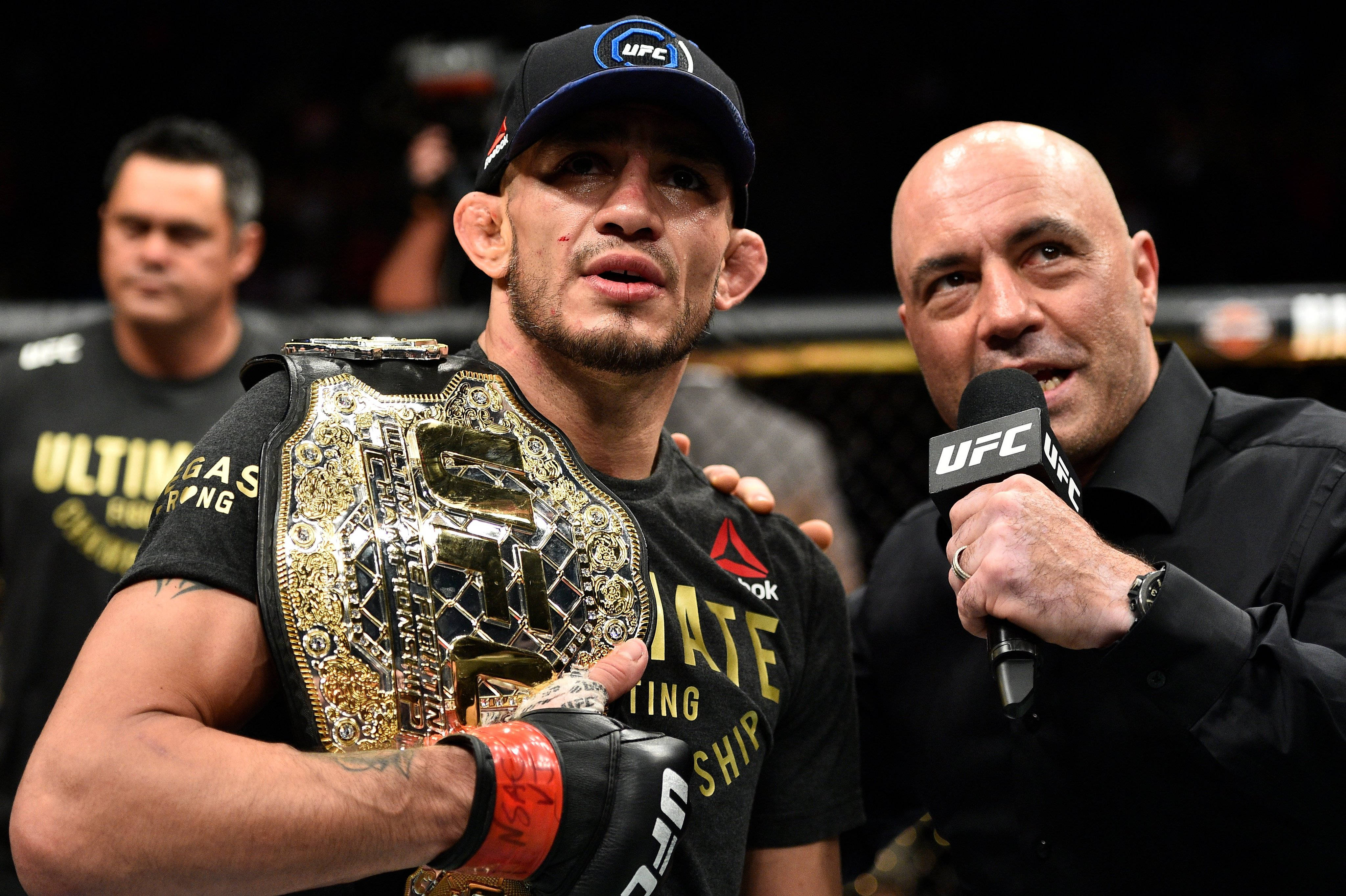 Champion 桌布 壁紙 — 一位勝利的UFC拳手在明亮的場館燈光下，於八角籠中接受訪問時手持冠軍腰帶。
