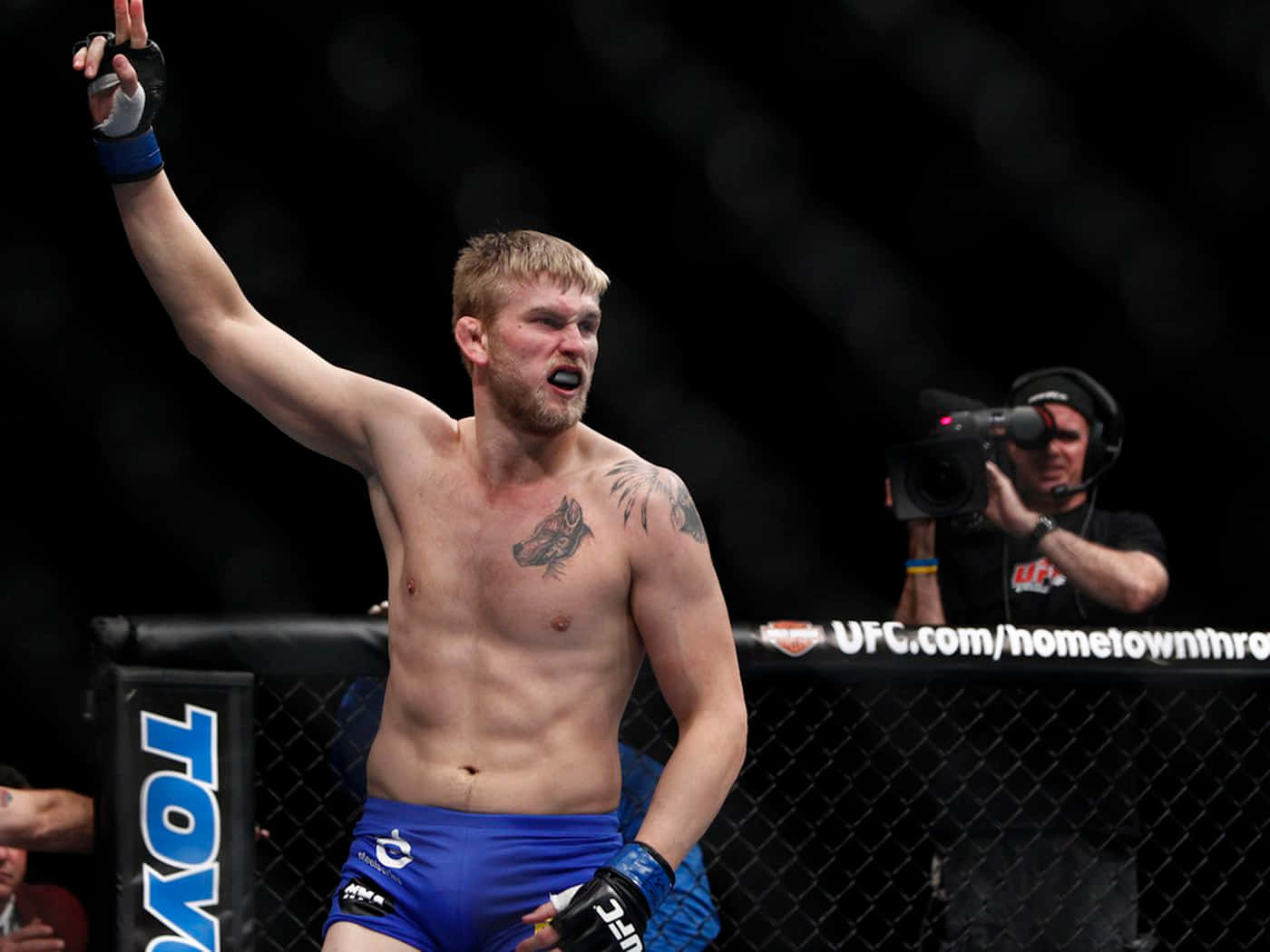 UFC 桌布 壁紙 — 一位勝利的UFC拳手在明亮的場館燈光下，於八角籠內高舉手臂慶祝勝利。