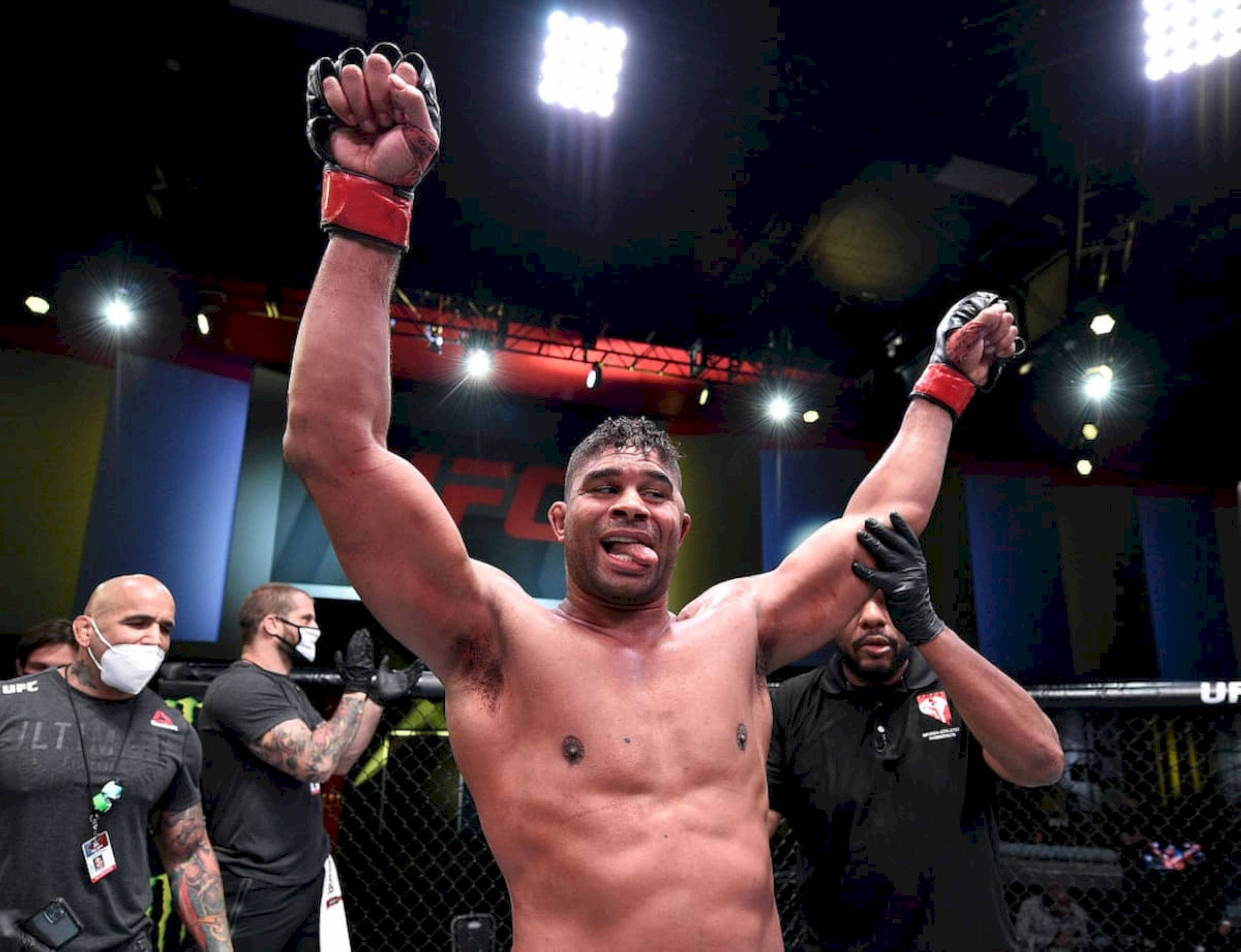 UFC 桌布 壁紙 — 一位勝利的UFC拳手在明亮的場館燈光下，於八角籠內高舉雙臂慶祝勝利。