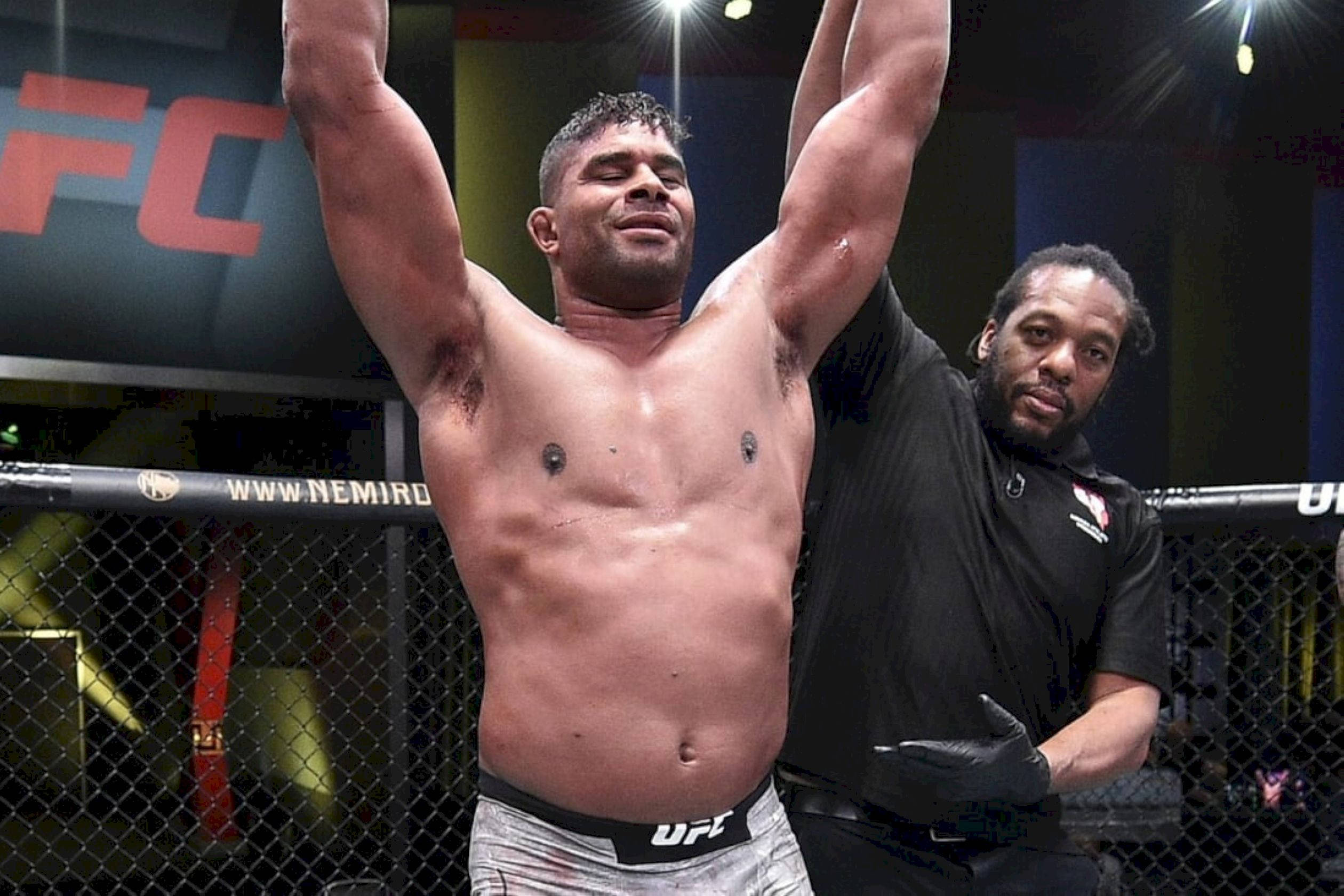 UFC 桌布 壁紙 — 一位勝利的UFC拳手在明亮的場館燈光下，於八角籠內高舉雙臂慶祝勝利，裁判握著他的手。