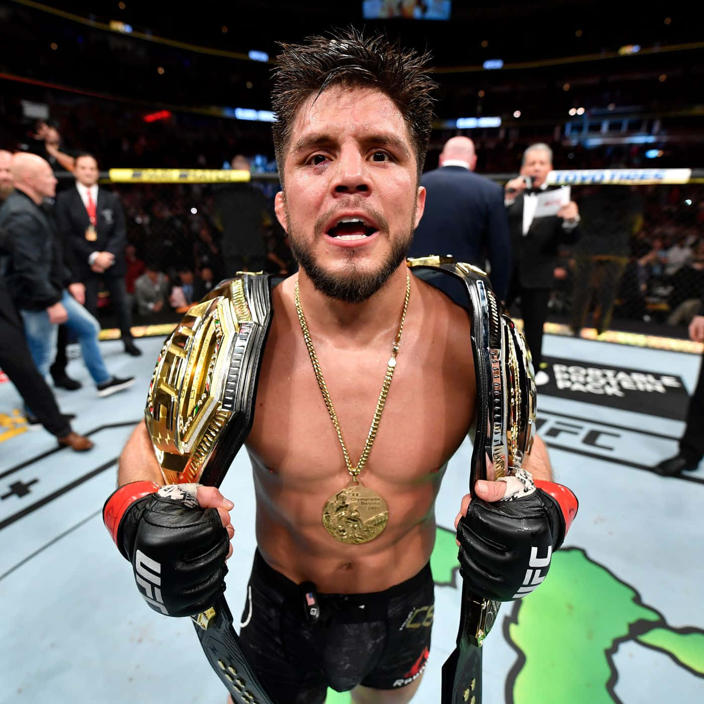 UFC 桌布 壁紙 — 一位勝利的UFC拳手在明亮的場館燈光下，於八角籠中自豪地展示他的冠軍腰帶。