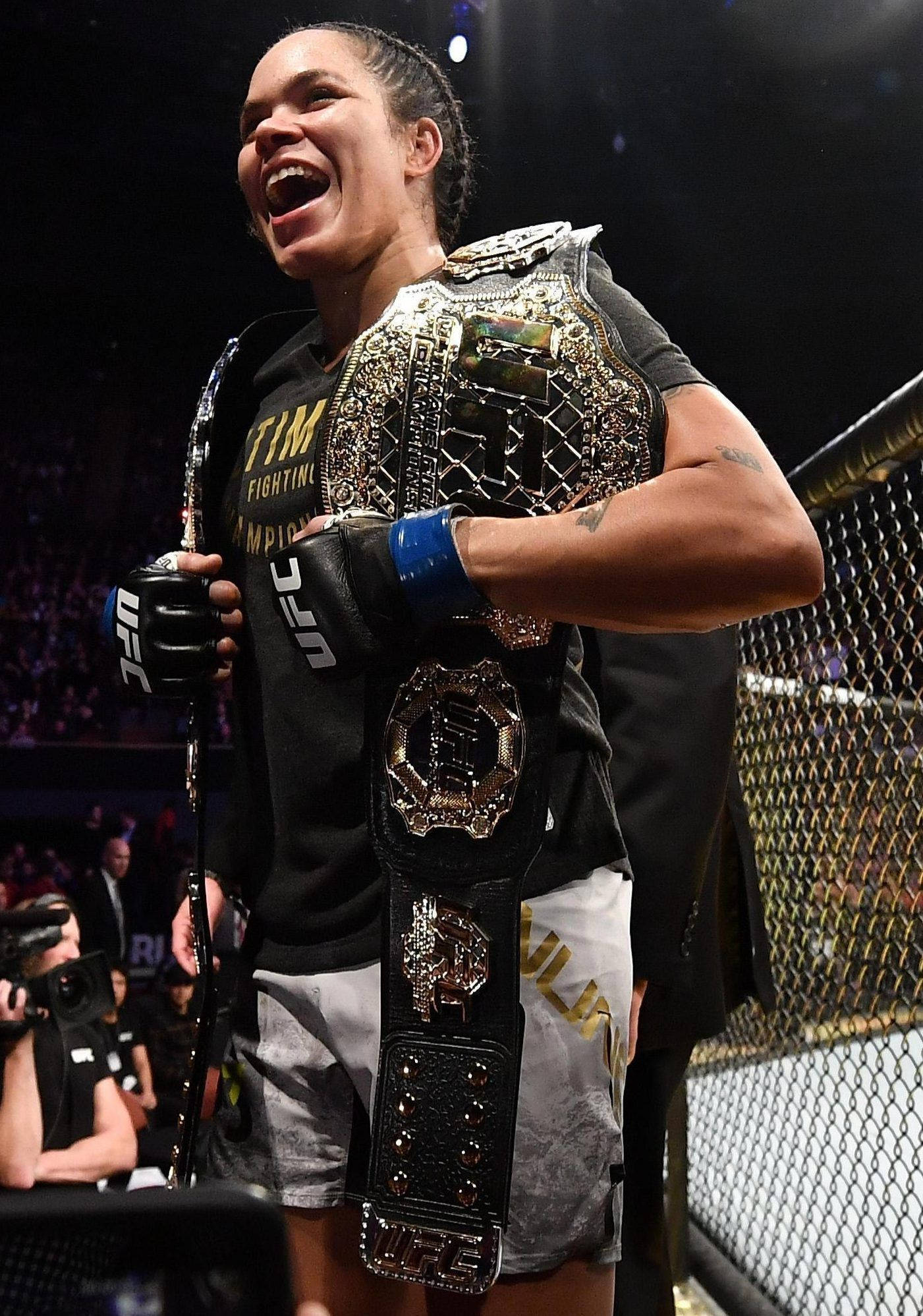 Champion 桌布 壁紙 — 一位勝利的UFC拳手在明亮的競技場燈光下，於八角籠內開心地笑著，手持她的冠軍腰帶。