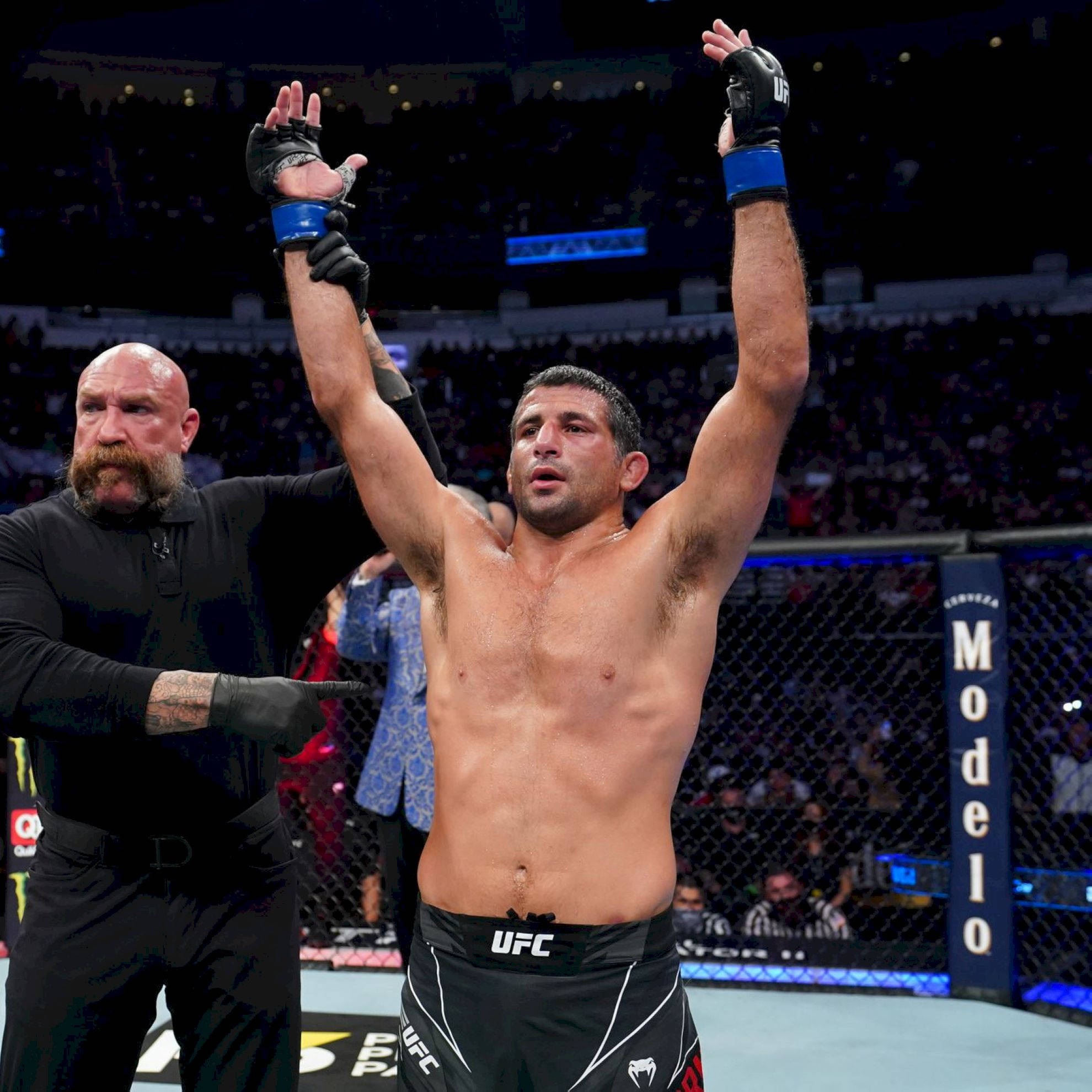 Victory 桌布 壁紙 — 一位勝利的UFC拳手在裁判於八角籠內宣布他為勝者時，高舉雙臂慶祝勝利。