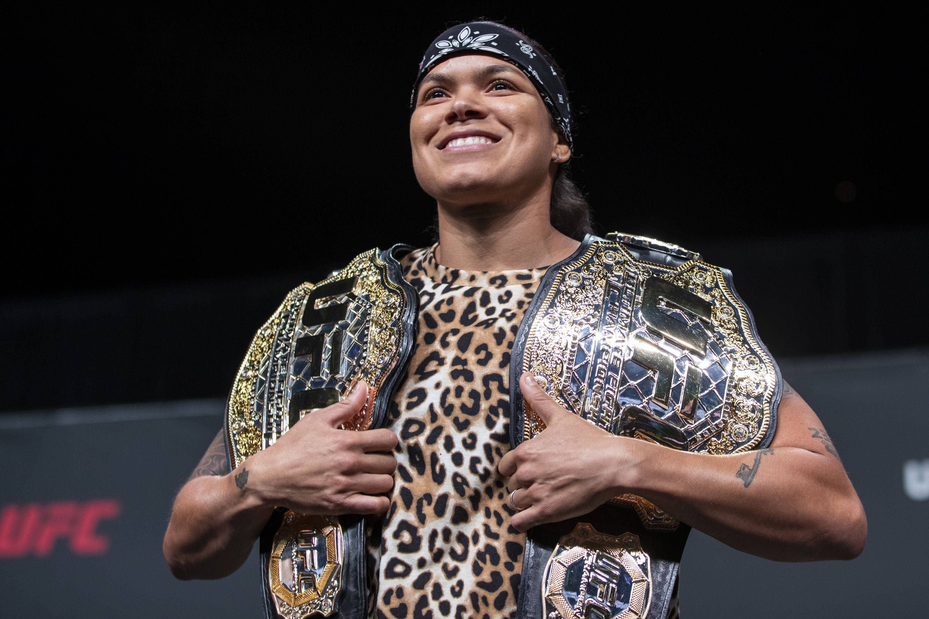 Champion 桌布 壁紙 — 一位勝利的UFC拳手在豹紋上衣上自豪地展示兩條冠軍腰帶，臉上洋溢著驕傲的笑容。