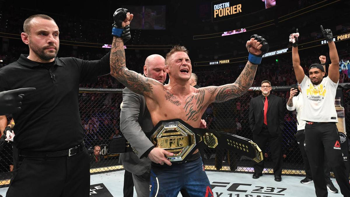 Victory 桌布 壁紙 — 一位勝利的UFC拳手帶有刺青，在八角籠內高舉冠軍腰帶，背景有裁判和人群，發出勝利的吶喊。