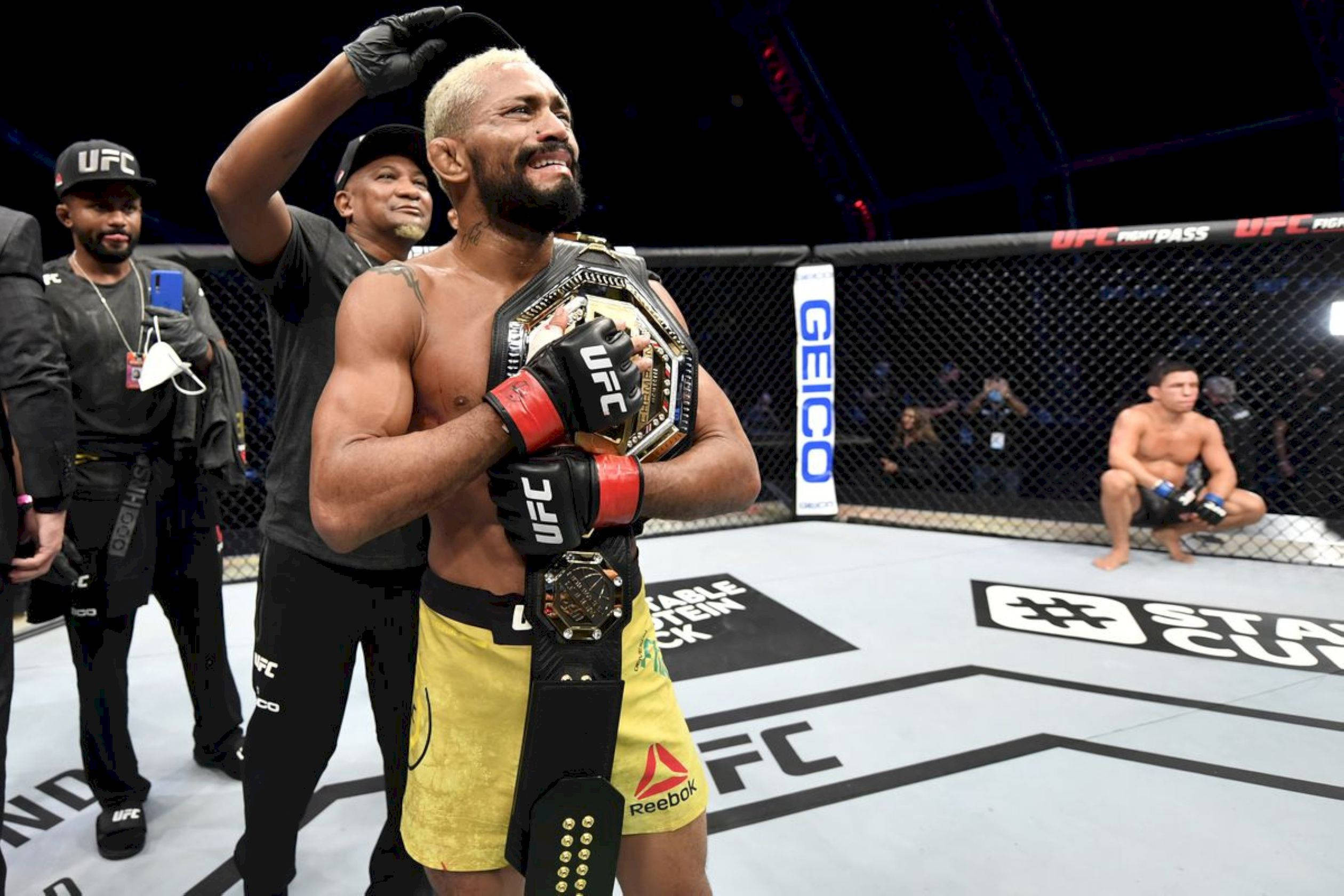 UFC 桌布 壁紙 — 一位勝利的UFC拳手帶著冠軍腰帶，在明亮的場館燈光下於八角籠中加冕時微笑。