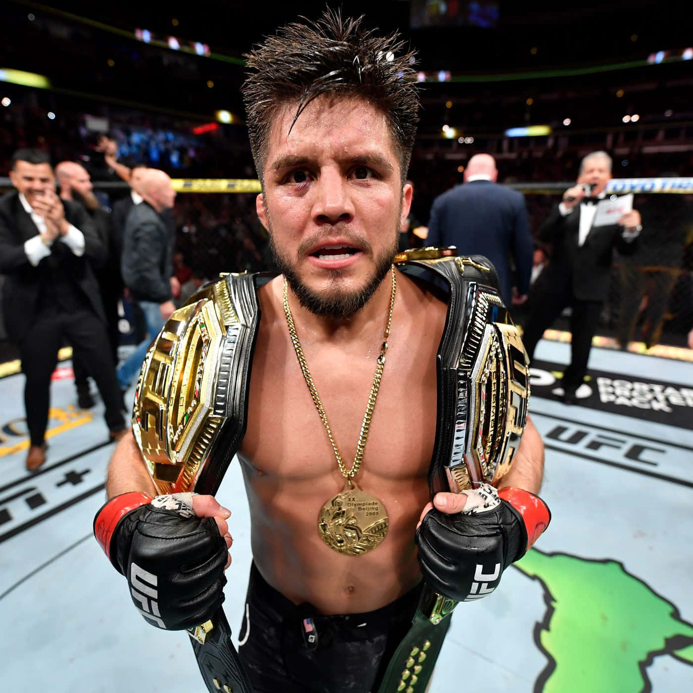 UFC 桌布 壁紙 — 一位勝利的UFC拳手站在八角籠中，手持兩條冠軍腰帶，脖子上掛著金牌。