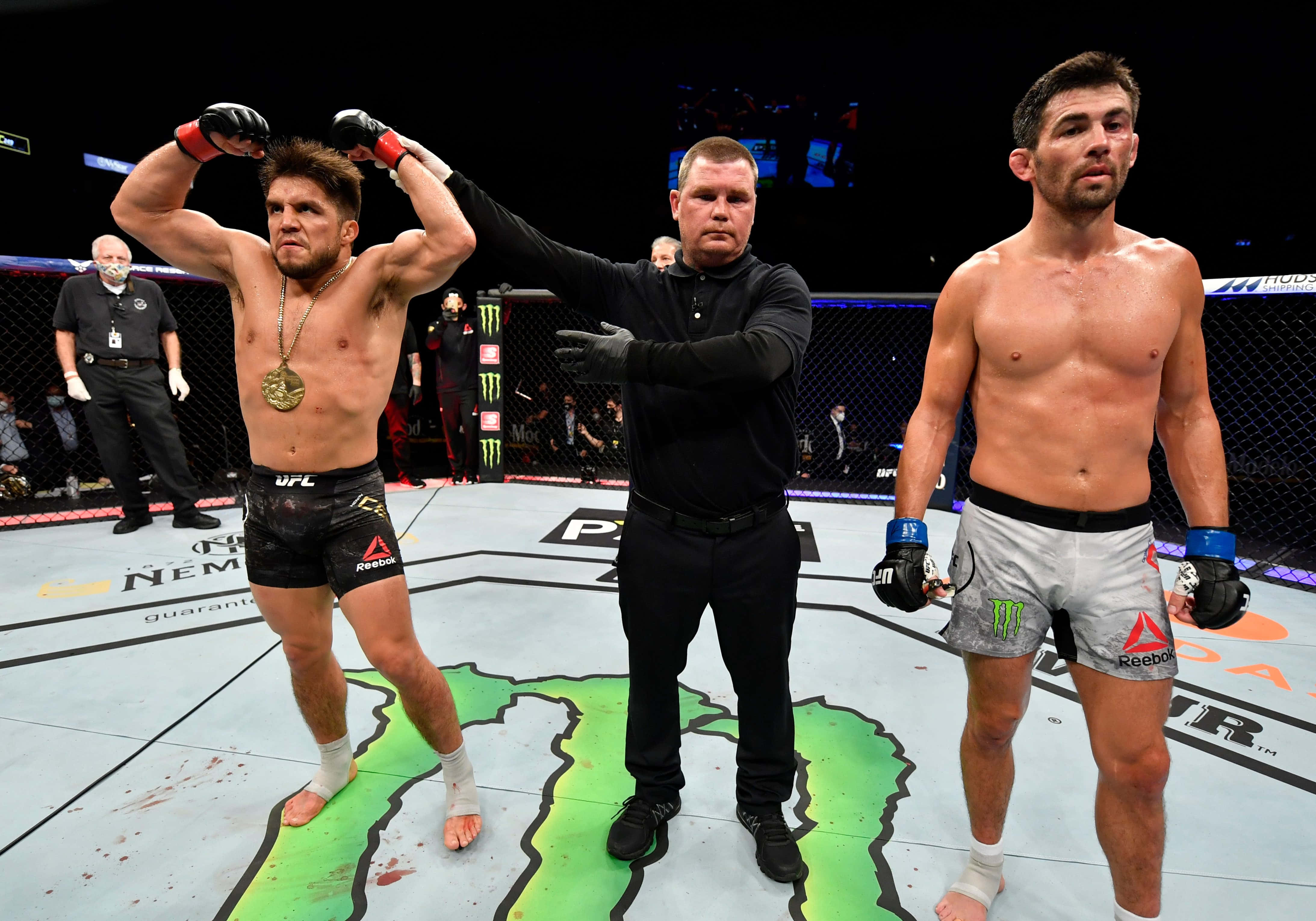 UFC 桌布 壁紙 — 一位勝利的UFC拳手高舉雙臂，裁判舉起他的手以示勝利，而他的對手則沮喪地站在八角籠中。
