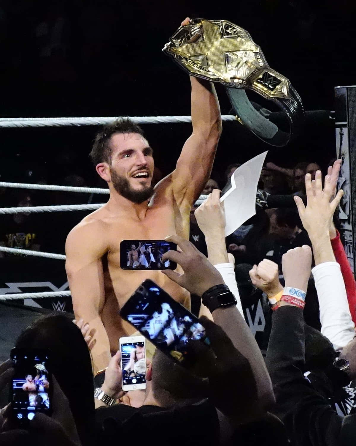WWE 桌布 壁紙 — 一位勝利的WWE摔角手在擂台上高舉閃亮的冠軍腰帶慶祝勝利，粉絲們用手機捕捉這一刻。