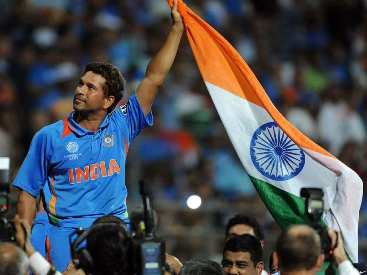 Sachin Tendulkar 桌布 壁紙 — 一位勝利的印度板球運動員身穿藍色球衣，在擠滿歡呼球迷的體育場中將三色旗高舉過頭頂。