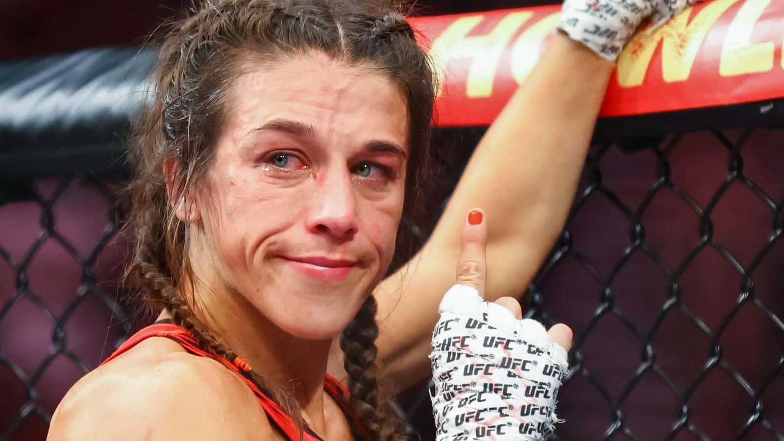 professional 桌布 壁紙 — 一位勝利的女性MMA拳手，編著辮子，戴著UFC手套，在八角籠內勝利微笑。
