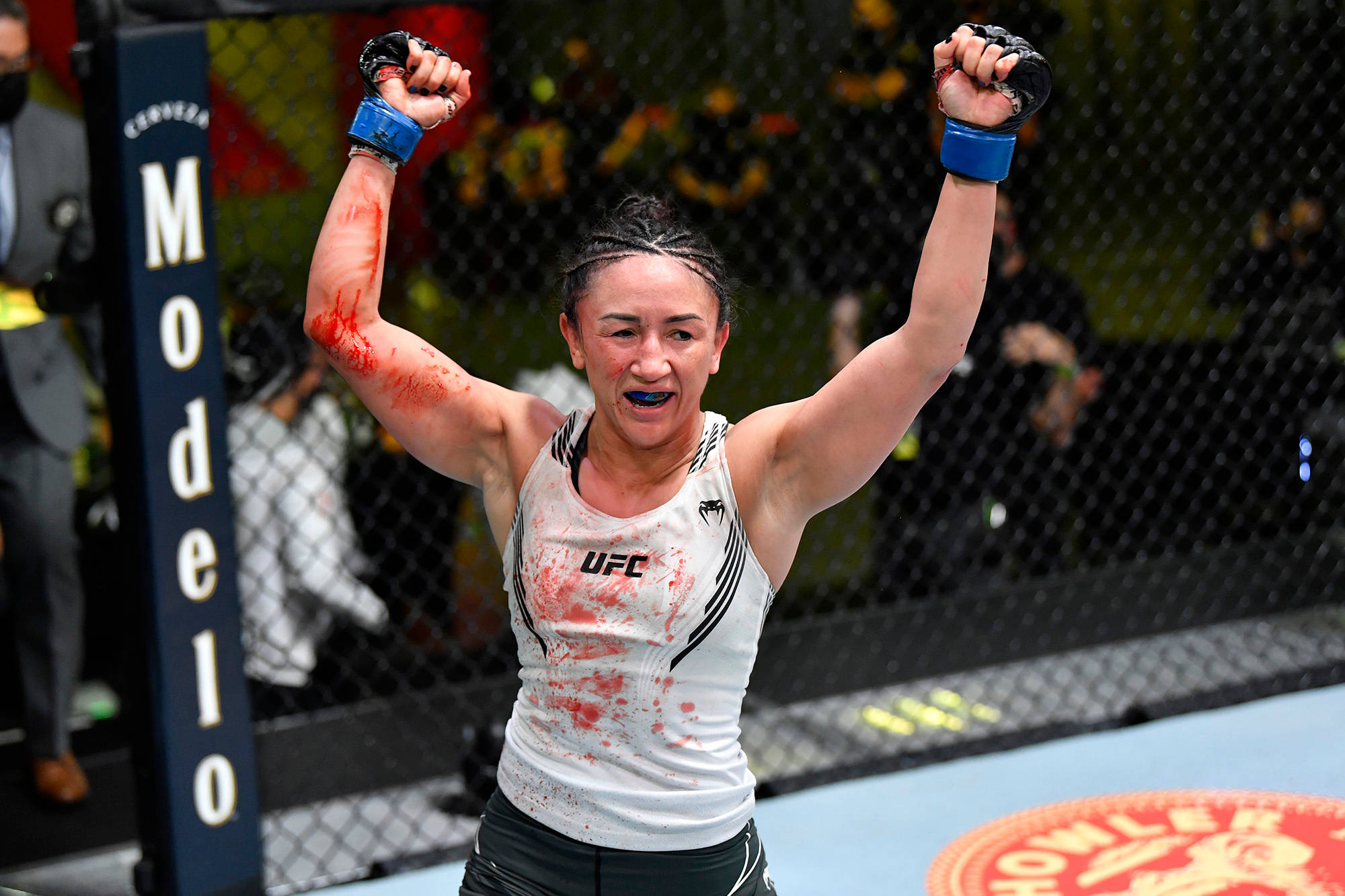 MMA 桌布 壁紙 — 一位勝利的女性MMA拳手在UFC賽事中，於血跡斑斑的八角籠內高舉拳頭慶祝勝利。