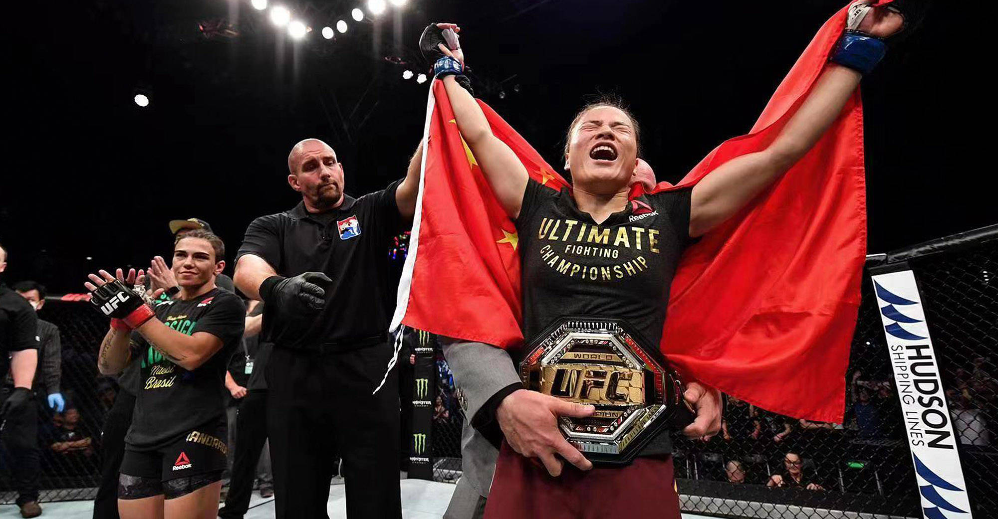 Champion 桌布 壁紙 — 一位勝利的女性MMA拳手在八角籠中手持冠軍腰帶並揮舞紅旗慶祝勝利。