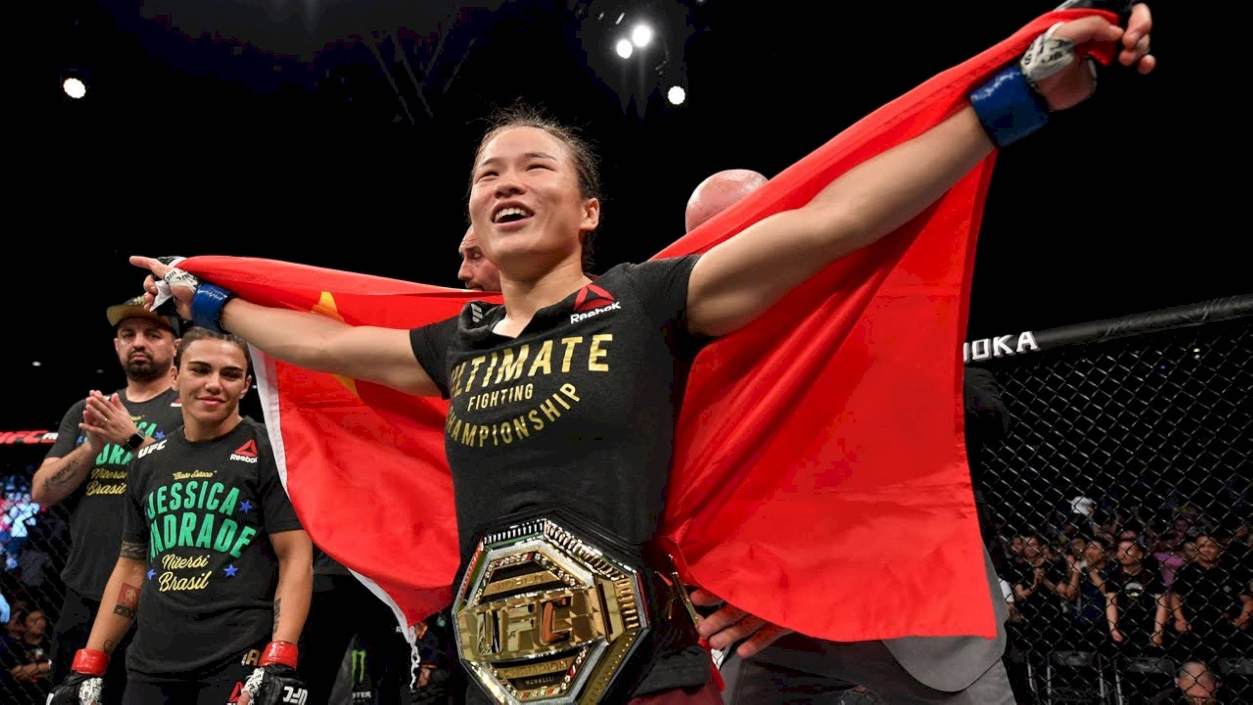 MMA 桌布 壁紙 — 一位勝利的女性MMA拳手在八角籠中手持冠軍腰帶並揮舞紅旗慶祝勝利。