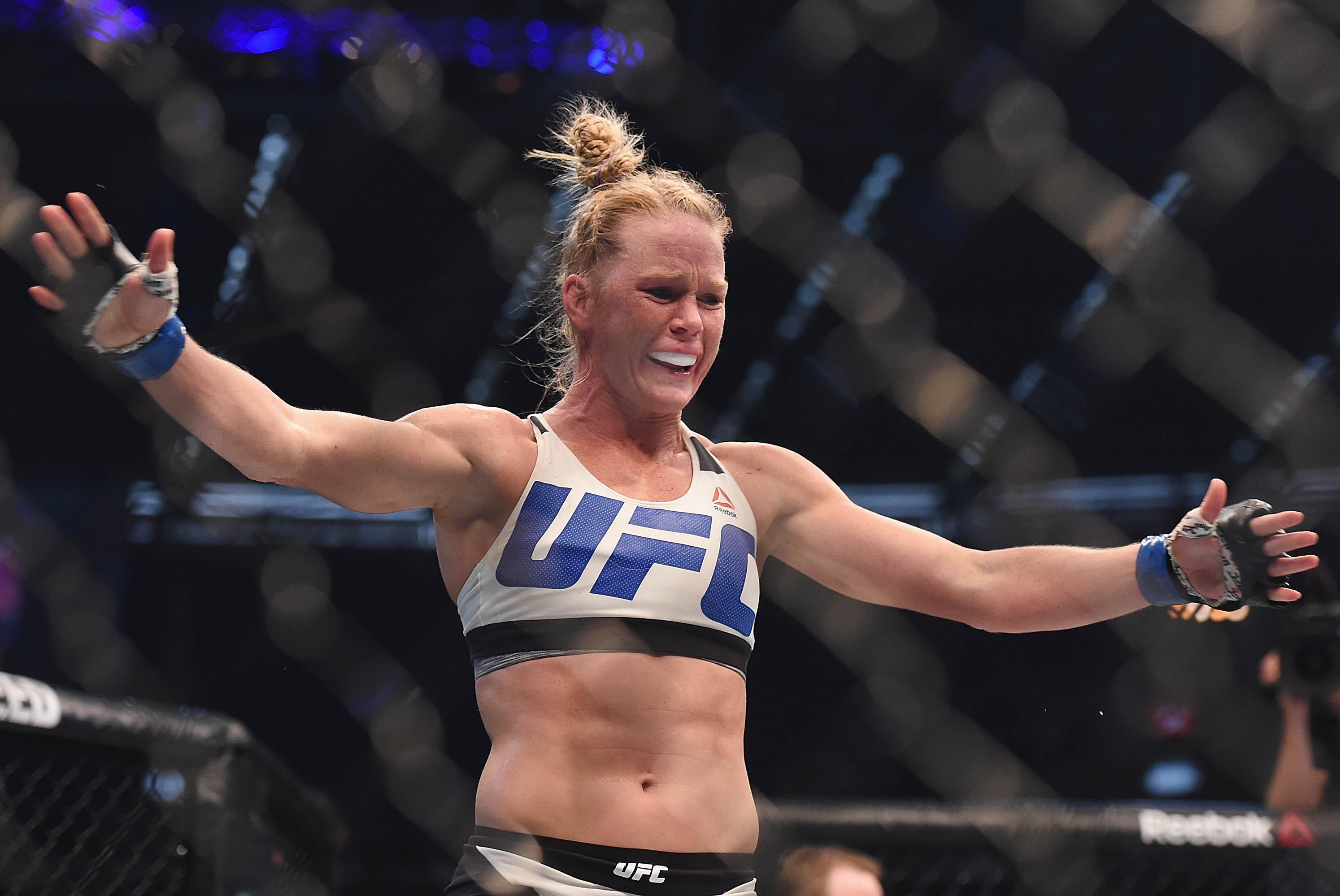 UFC 桌布 壁紙 — 一位勝利的女性UFC拳手在八角籠中張開雙臂，帶著喜悅的表情慶祝勝利。