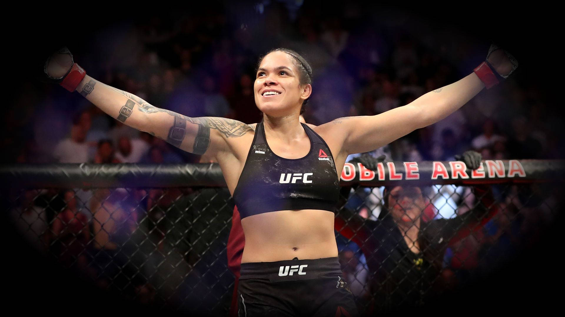 Victory 桌布 壁紙 — 一位勝利的女性UFC拳手在八角籠內，於場館燈光下高舉雙臂慶祝勝利。