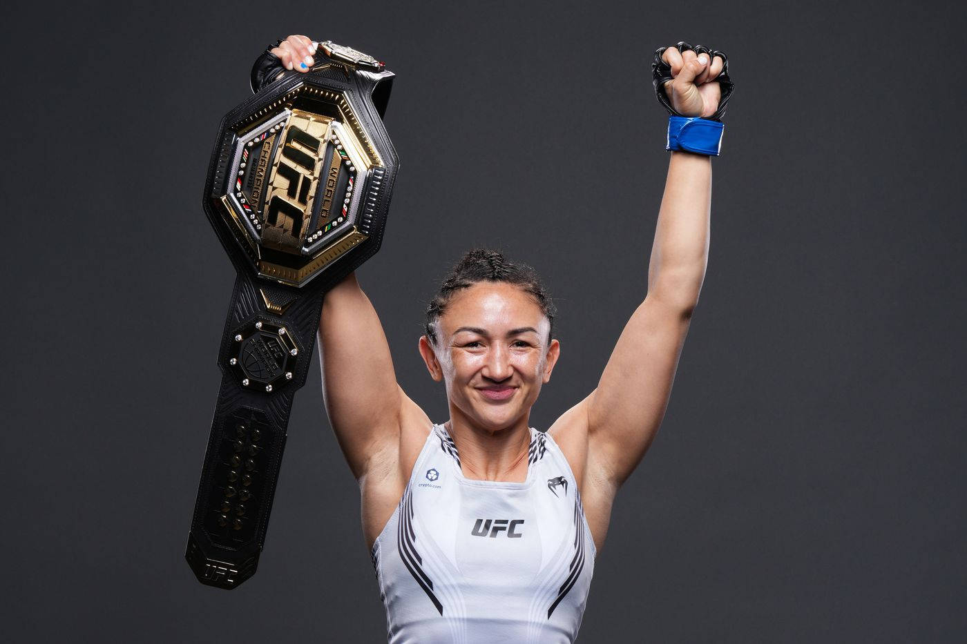 Champion 桌布 壁紙 — 一位勝利的女性UFC拳擊手在黑暗的攝影棚背景下高舉冠軍腰帶和緊握的拳頭慶祝勝利。