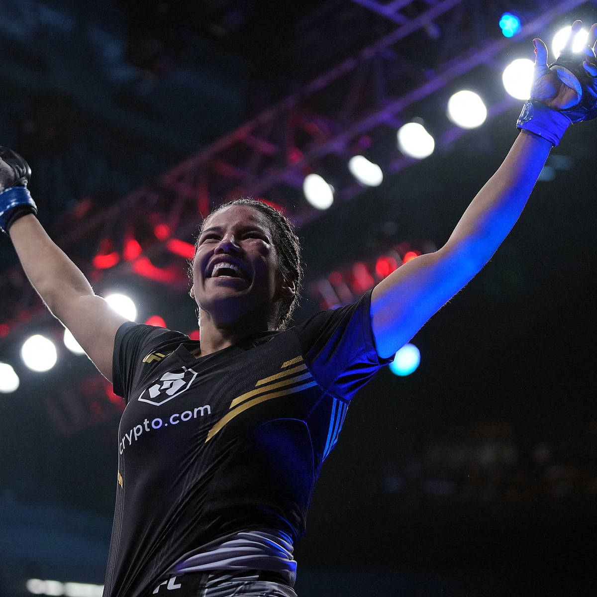 MMA 桌布 壁紙 — 一位勝利的女性戰士在明亮的競技場燈光下高舉雙臂慶祝勝利。