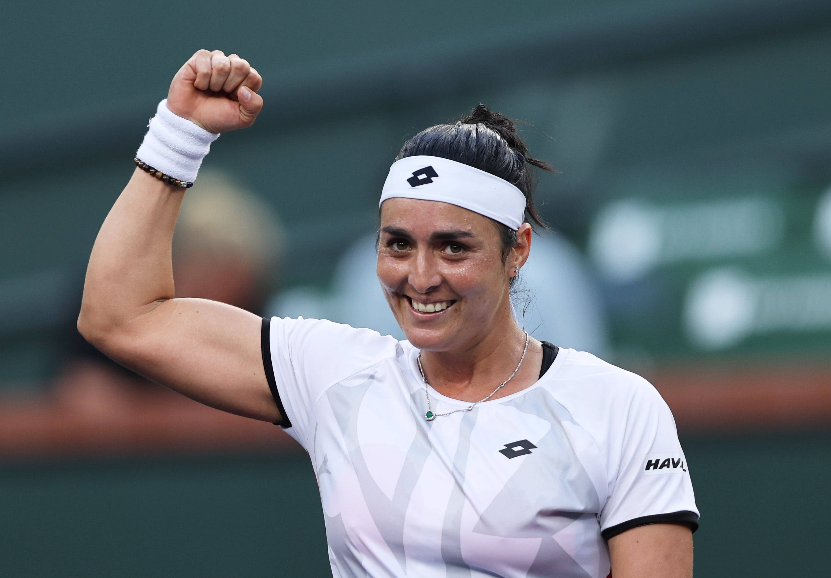 Athletic 桌布 壁紙 — 一位勝利的女性網球選手在綠色球場上高舉緊握的拳頭慶祝勝利，露出燦爛的笑容。