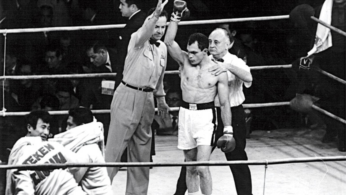 Boxing 桌布 壁紙 — 一位勝利的拳擊手在復古拳擊擂台上被裁判舉起，而他被打敗的對手正在接受治療。