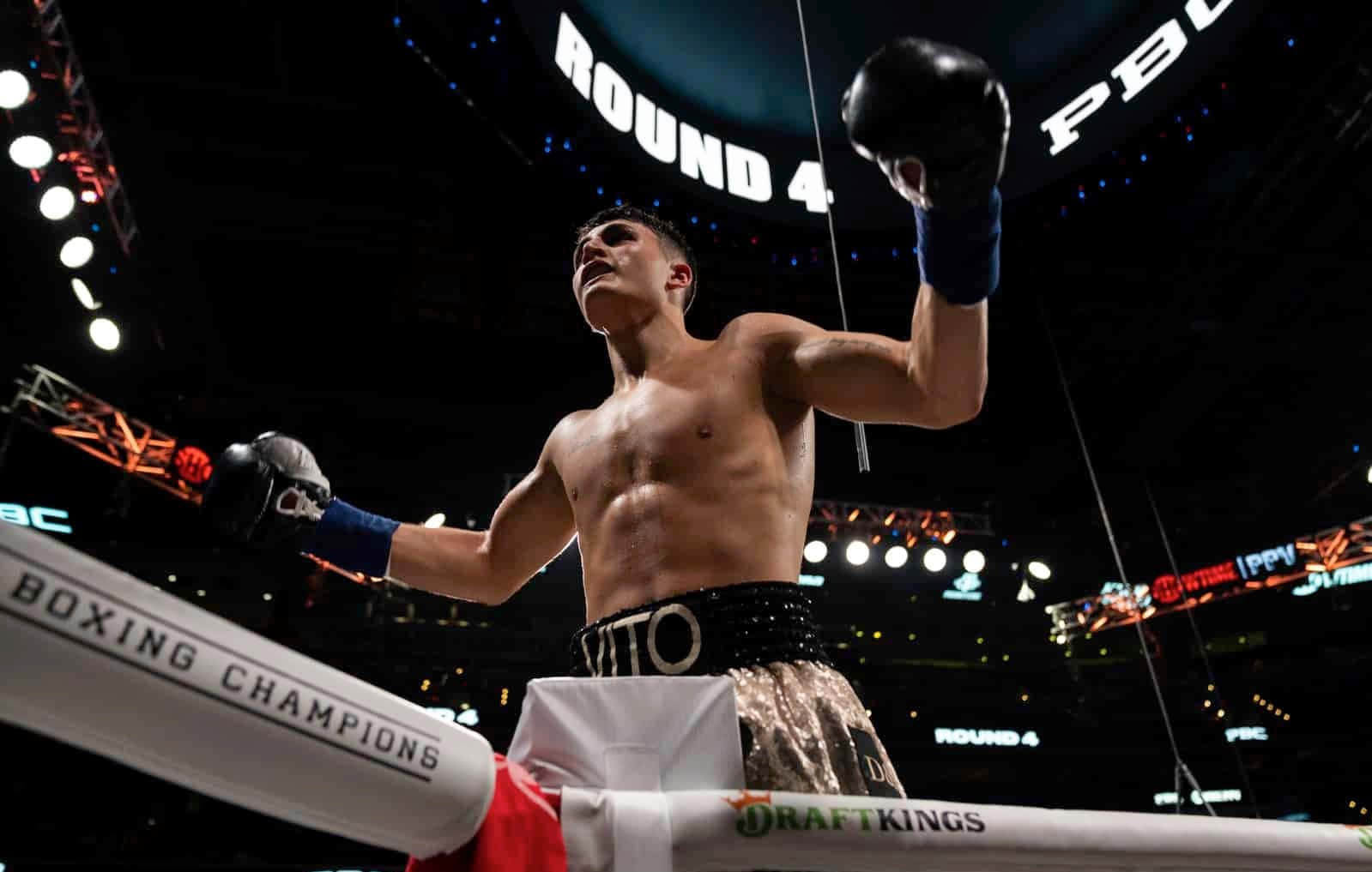 Ryan Garcia 桌布 壁紙 — 一位勝利的拳擊手在職業比賽的第四回合中，在燈光明亮的拳擊台上舉起戴著手套的拳頭慶祝勝利。